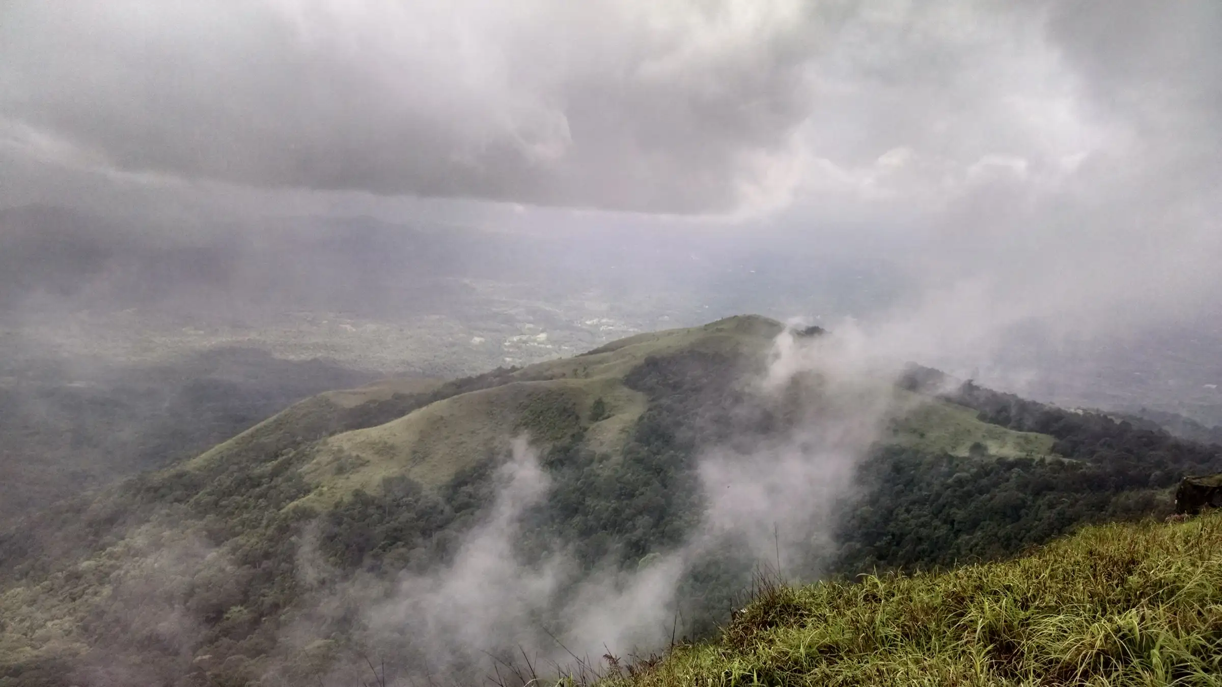 Cloud drifting over a forested green ridge seen from near Kurinjal peak