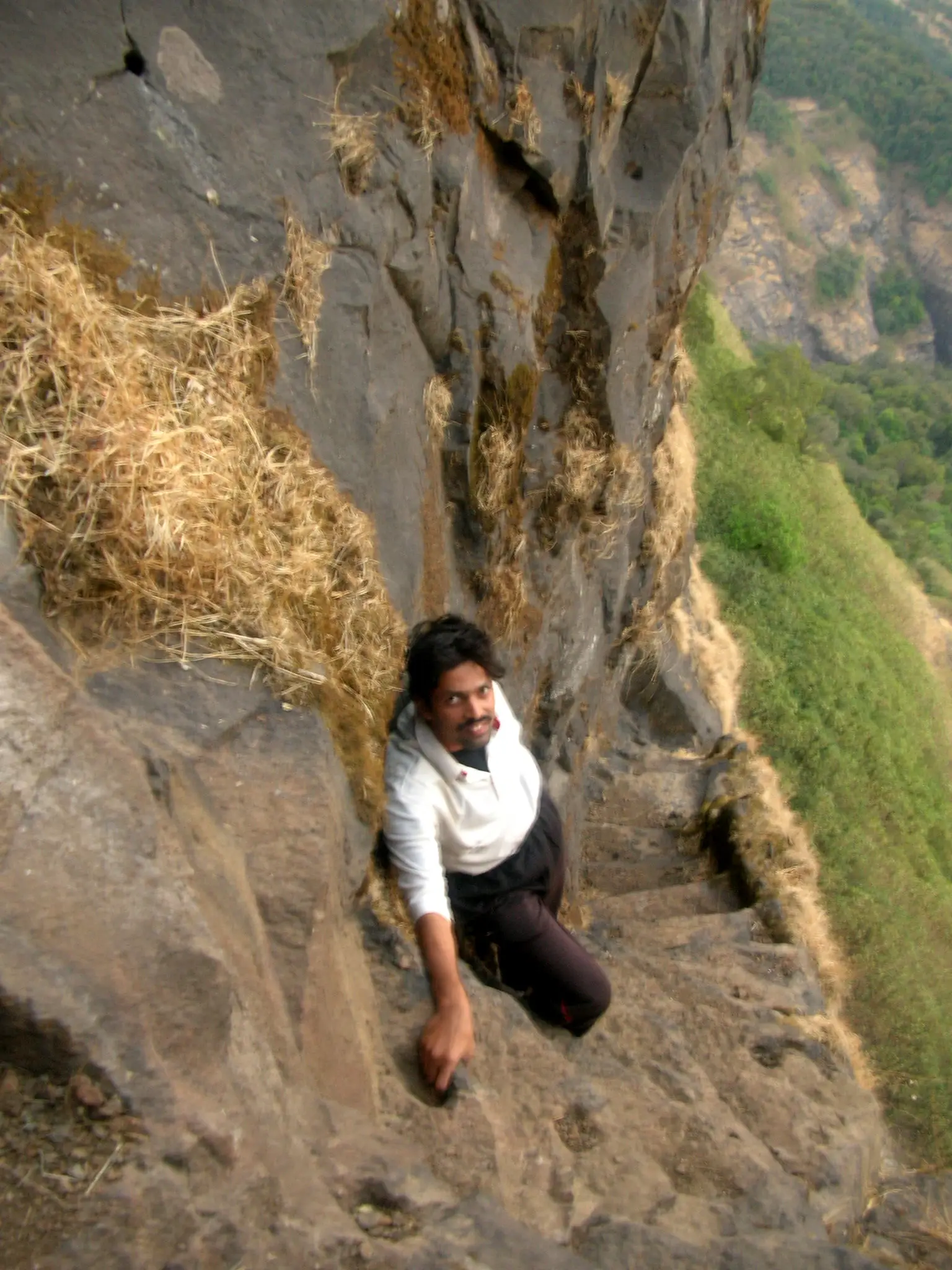 Trekker climbing narrow rock-cut steps on Alang Fort with a steep drop to the valley alongside