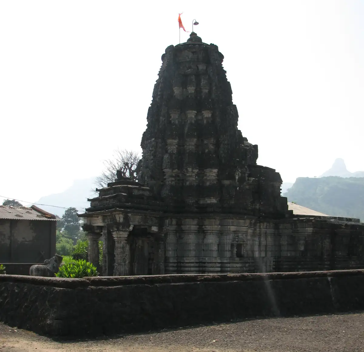 Dark carved stone shikhara of the Amruteshwar temple at Ratanwadi with a saffron flag on top
