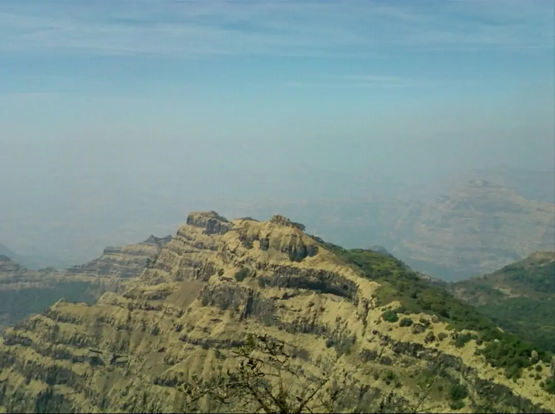 Layered basalt cliff with scrub at Arthur's Seat, Mahabaleshwar, above a hazy valley