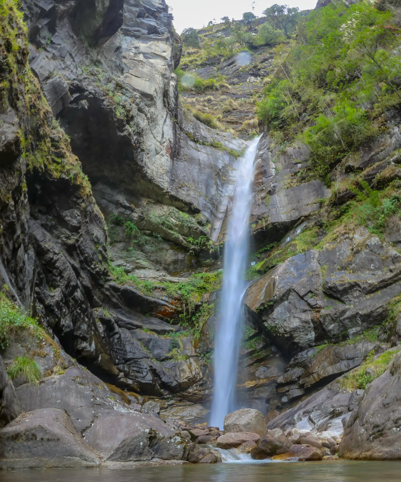 Tall thin waterfall dropping into a rocky pool in a grey rock gorge at the Atri Muni cave