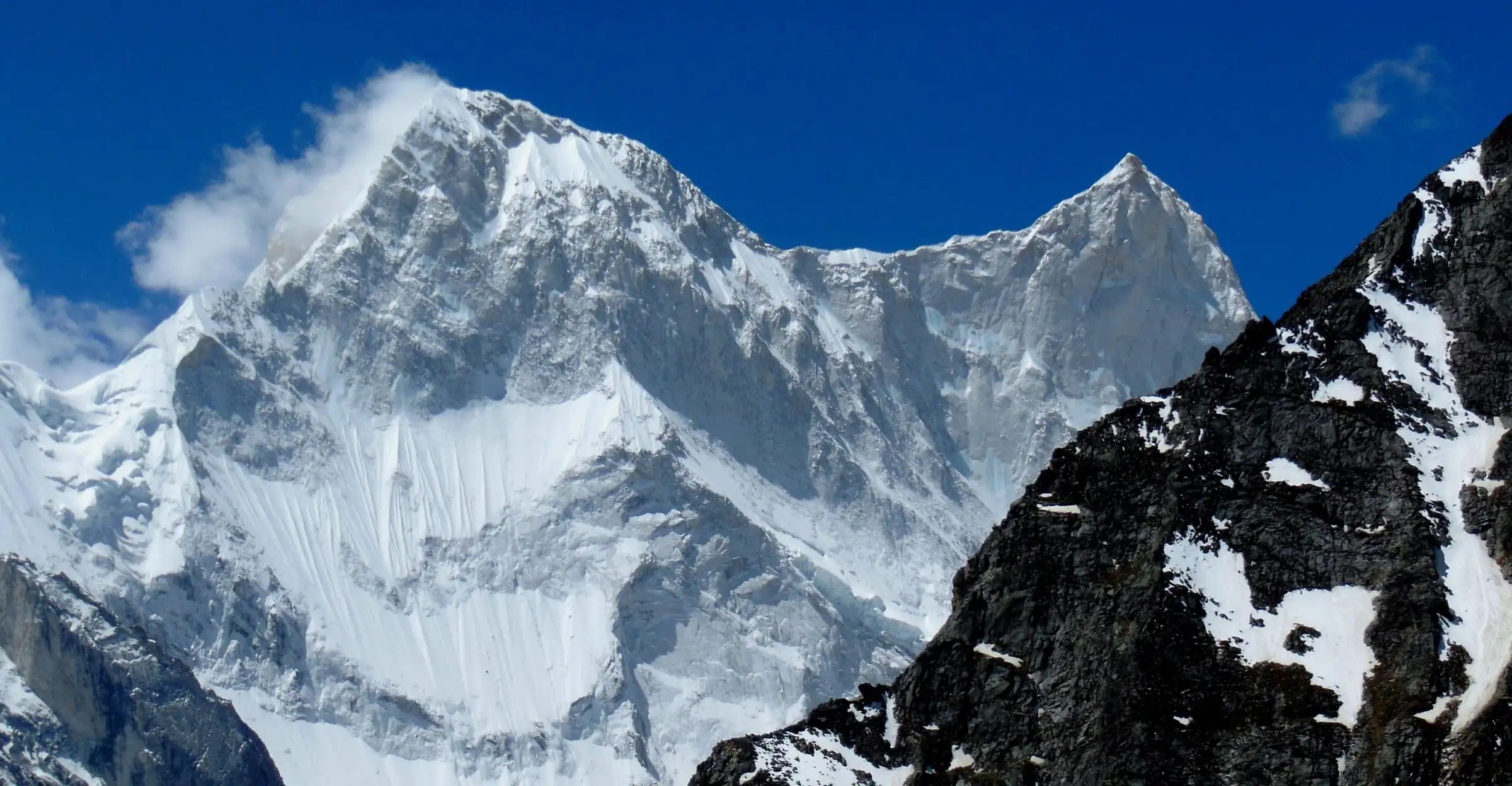 Snow-plastered Kalanka and Changabang peaks above a dark rocky ridge, seen from the Bagini Glacier side trip