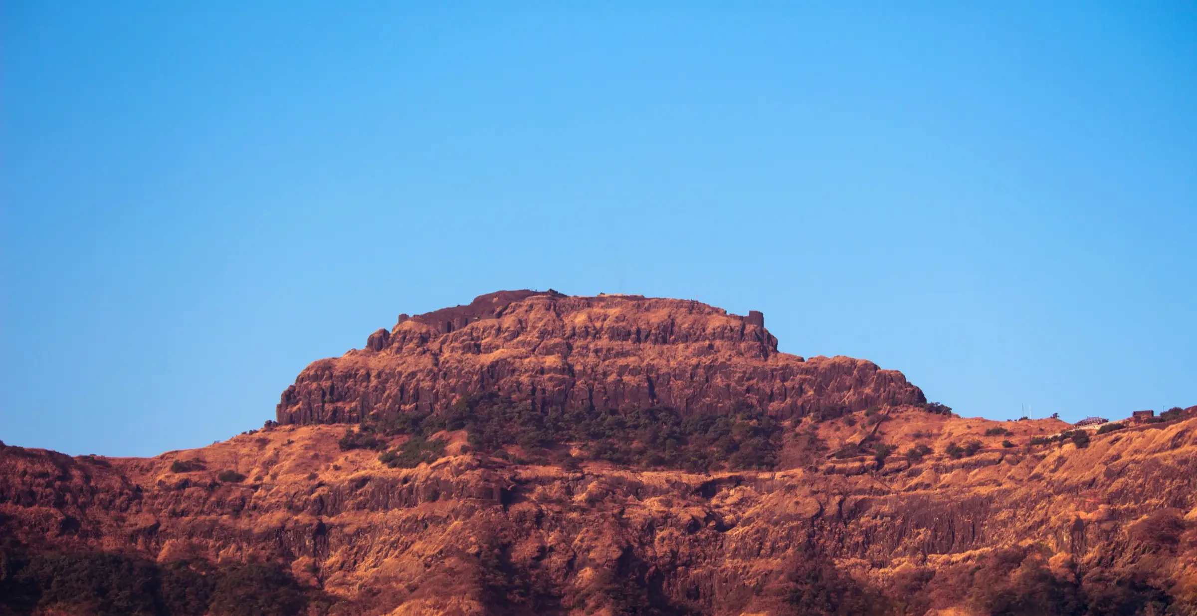 The rocky Balekilla citadel of Rajgad rising above dry brown slopes under a clear blue sky