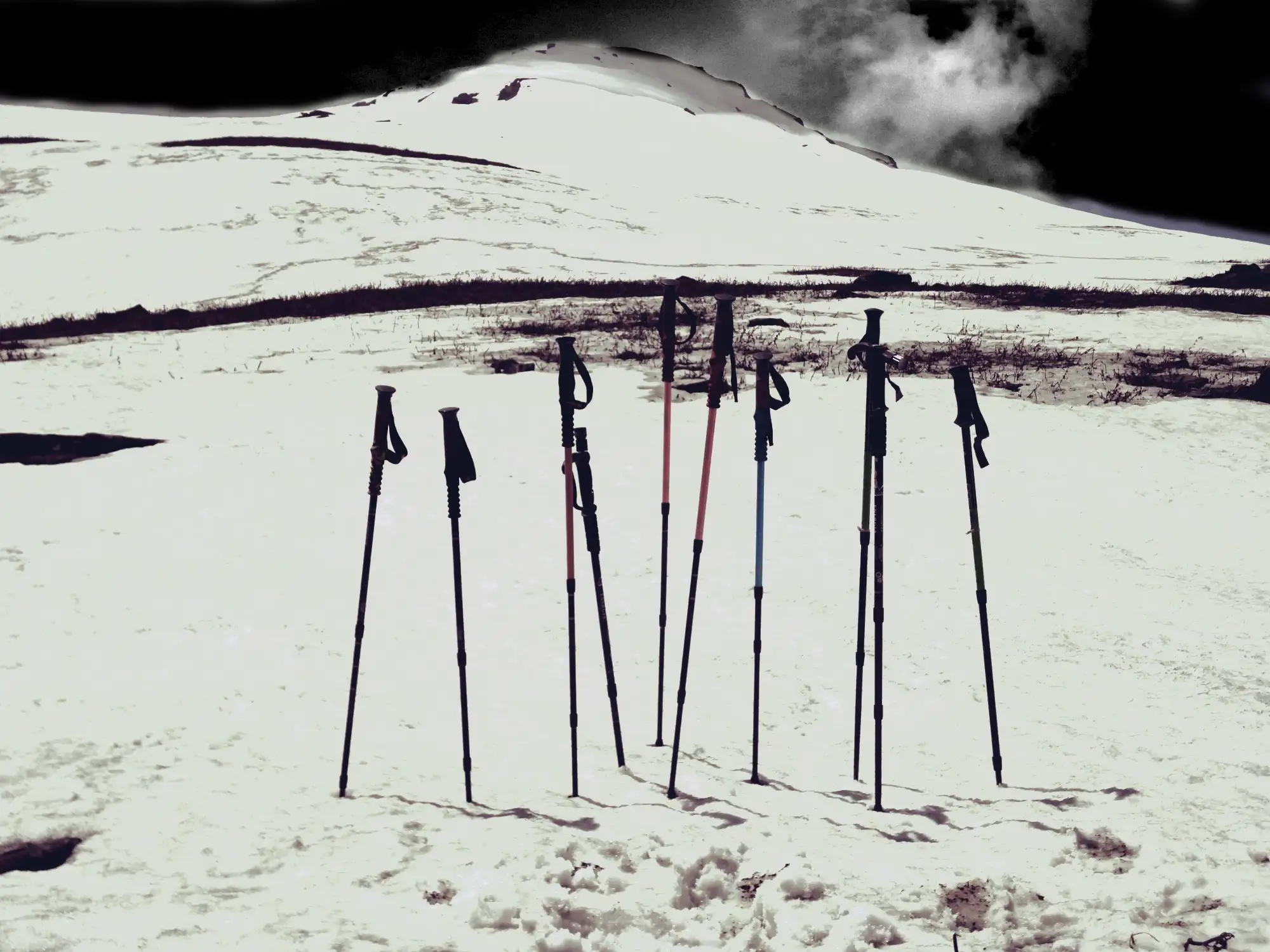 Trekking poles standing in snow below the white slope of Baluni Top on the Sunderdhunga trek