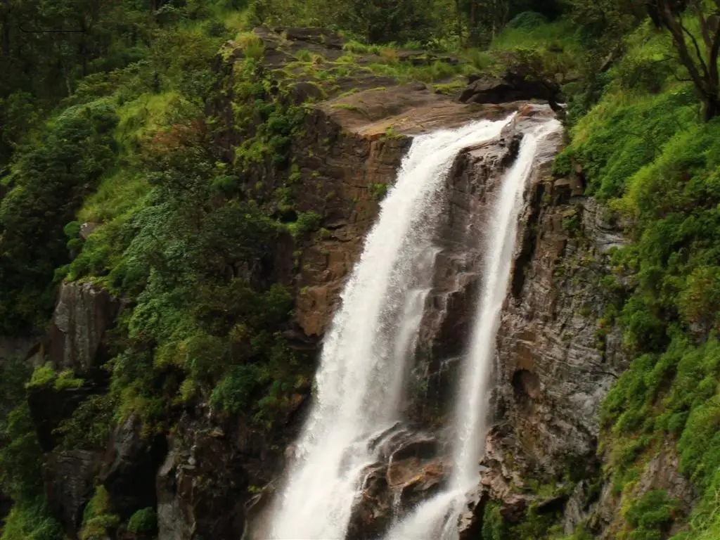 Bandaje Falls pouring over a dark rock lip, the waterfall reached by the extension trail beyond the fort