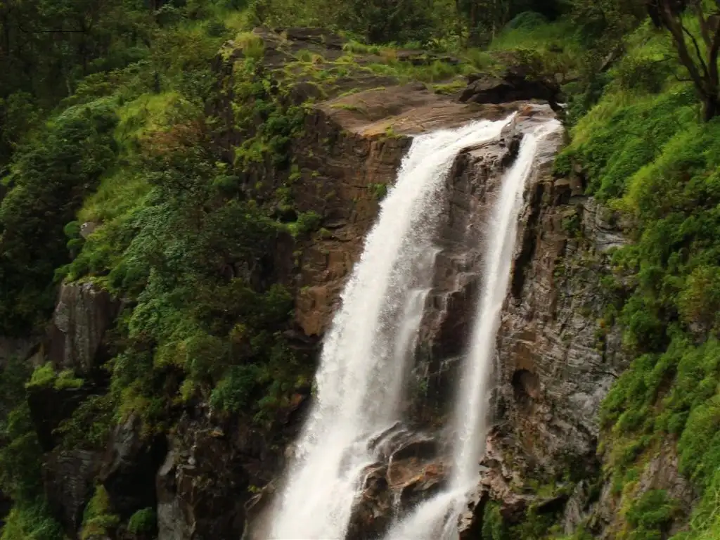 Bandaje Falls pouring over a dark rock lip, the waterfall reached by the extension trail beyond the fort