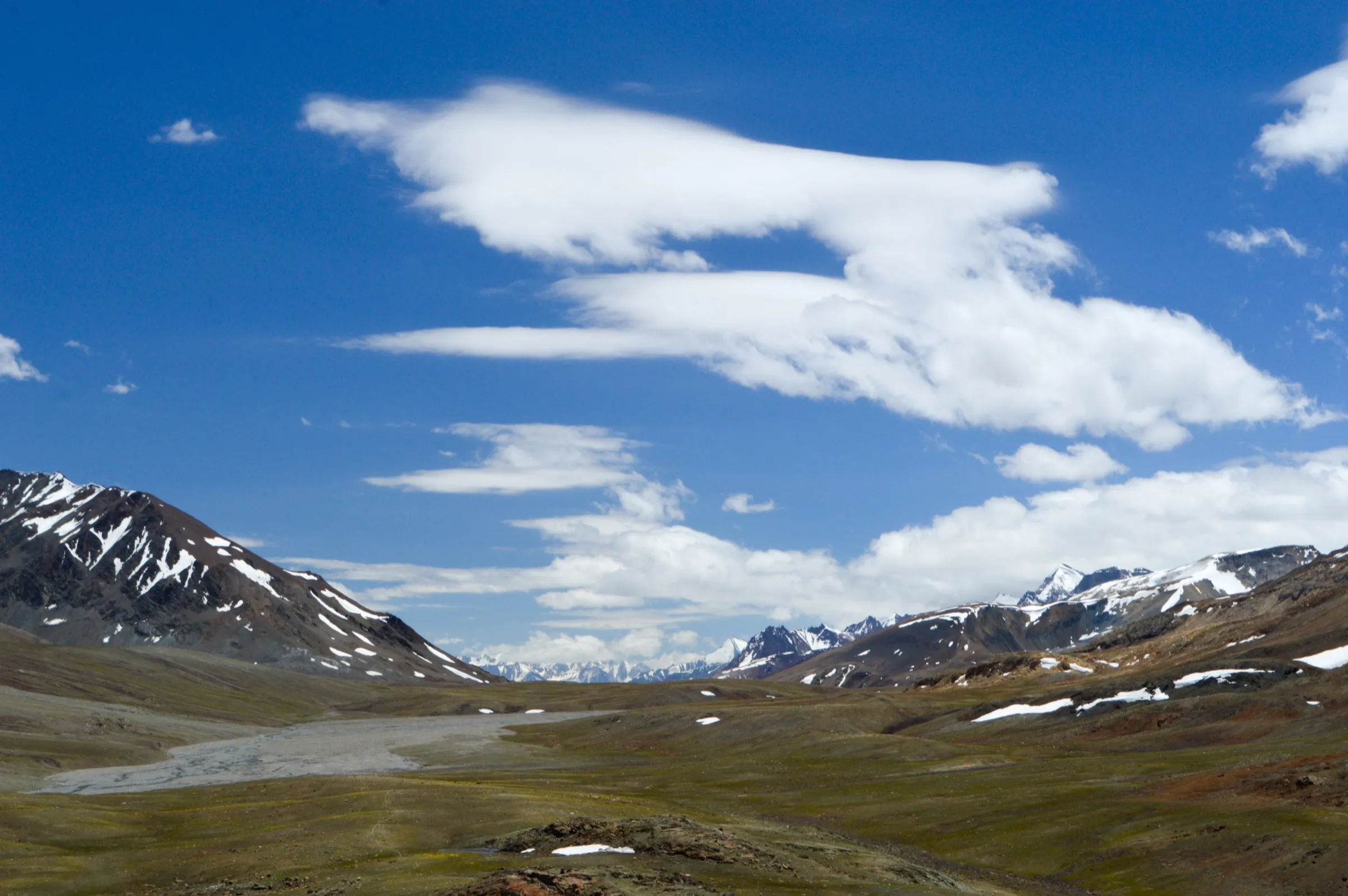 Open cold-desert meadows and a braided glacial stream below snow-streaked peaks at Baralacha La, where the Chandrabhaga Glaciers trek begins