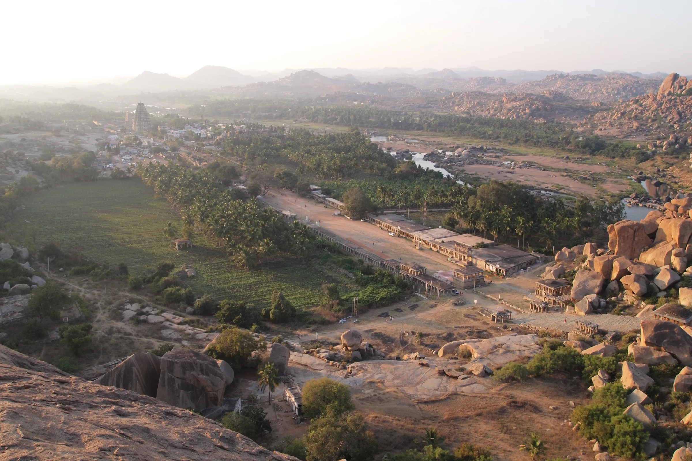 View from Matanga Hill over boulders to the long Hampi Bazaar street, the Virupaksha temple tower and coconut groves at sunset