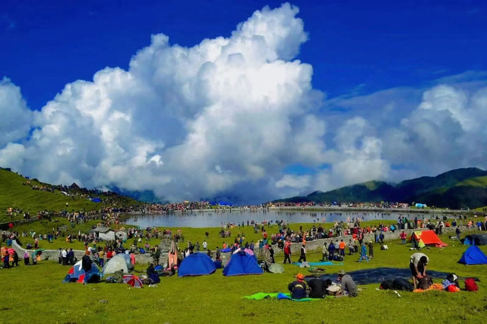 Thousands of pilgrims and tents around Bedni Kund on the green Bedni Bugyal meadow under towering white clouds