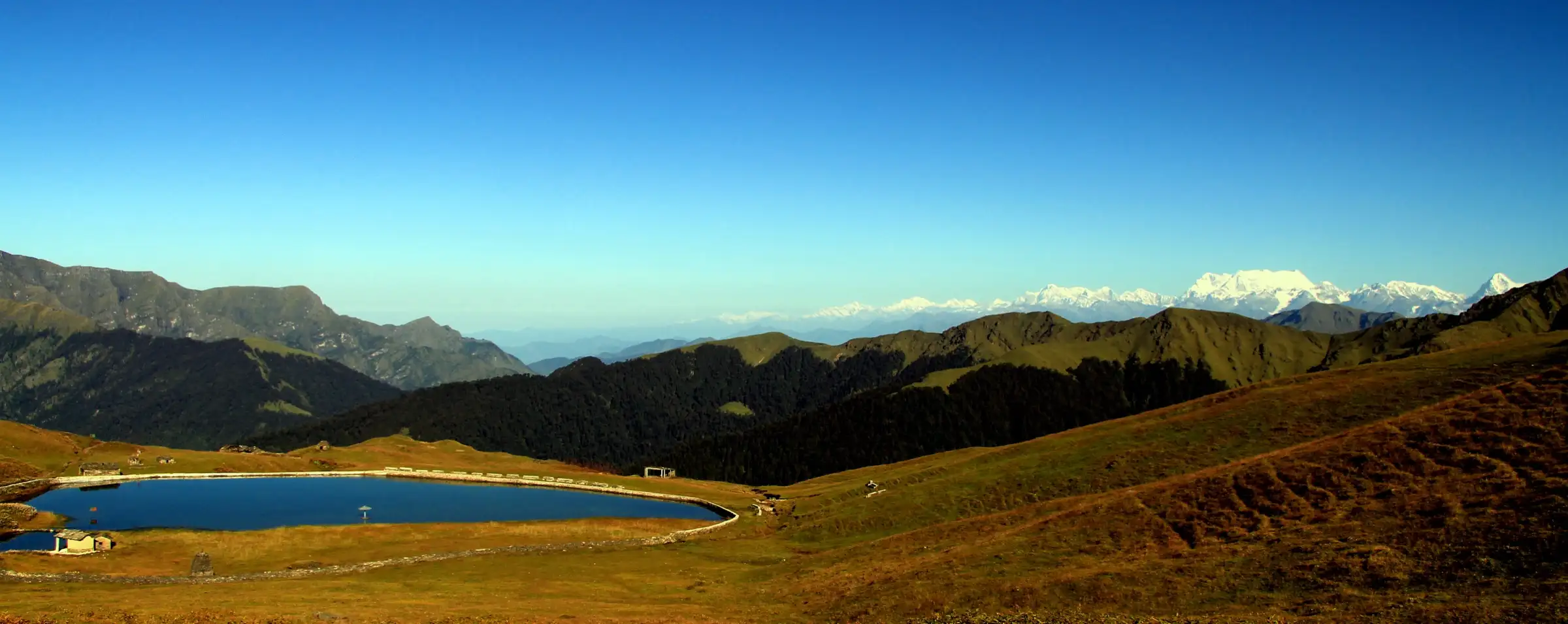 Bedni Kund pond on the brown autumn meadow with a row of snow peaks on the horizon