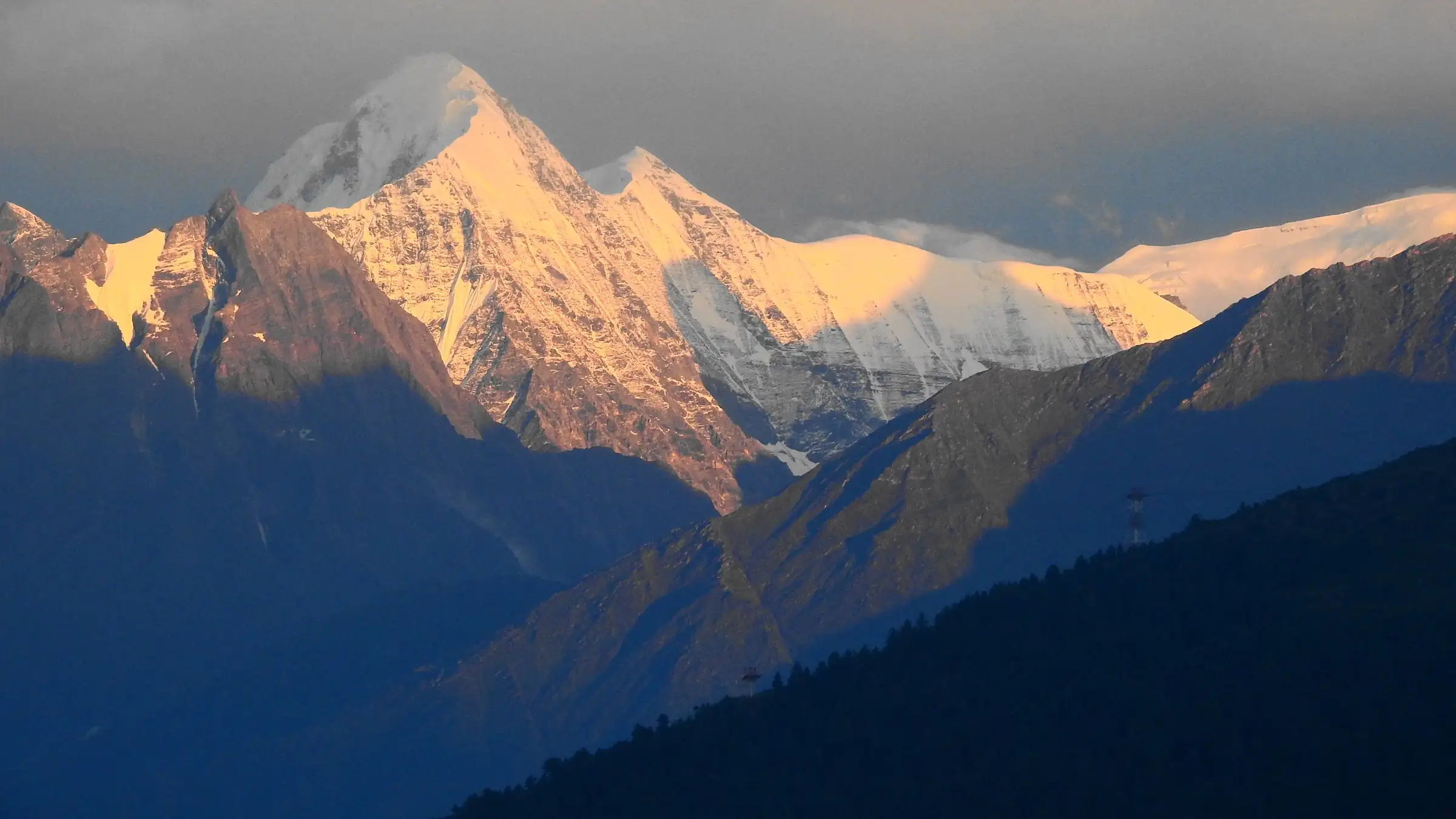 Snow peak of Bethartoli glowing gold at sunrise above dark ridges, seen from Thaing village