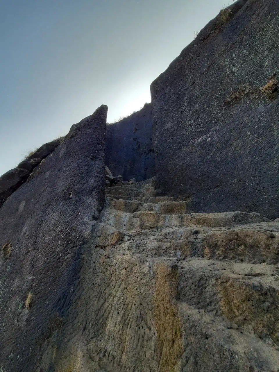 Worn rock-cut steps climbing through a narrow cleft between dark basalt walls on Bhaskargad