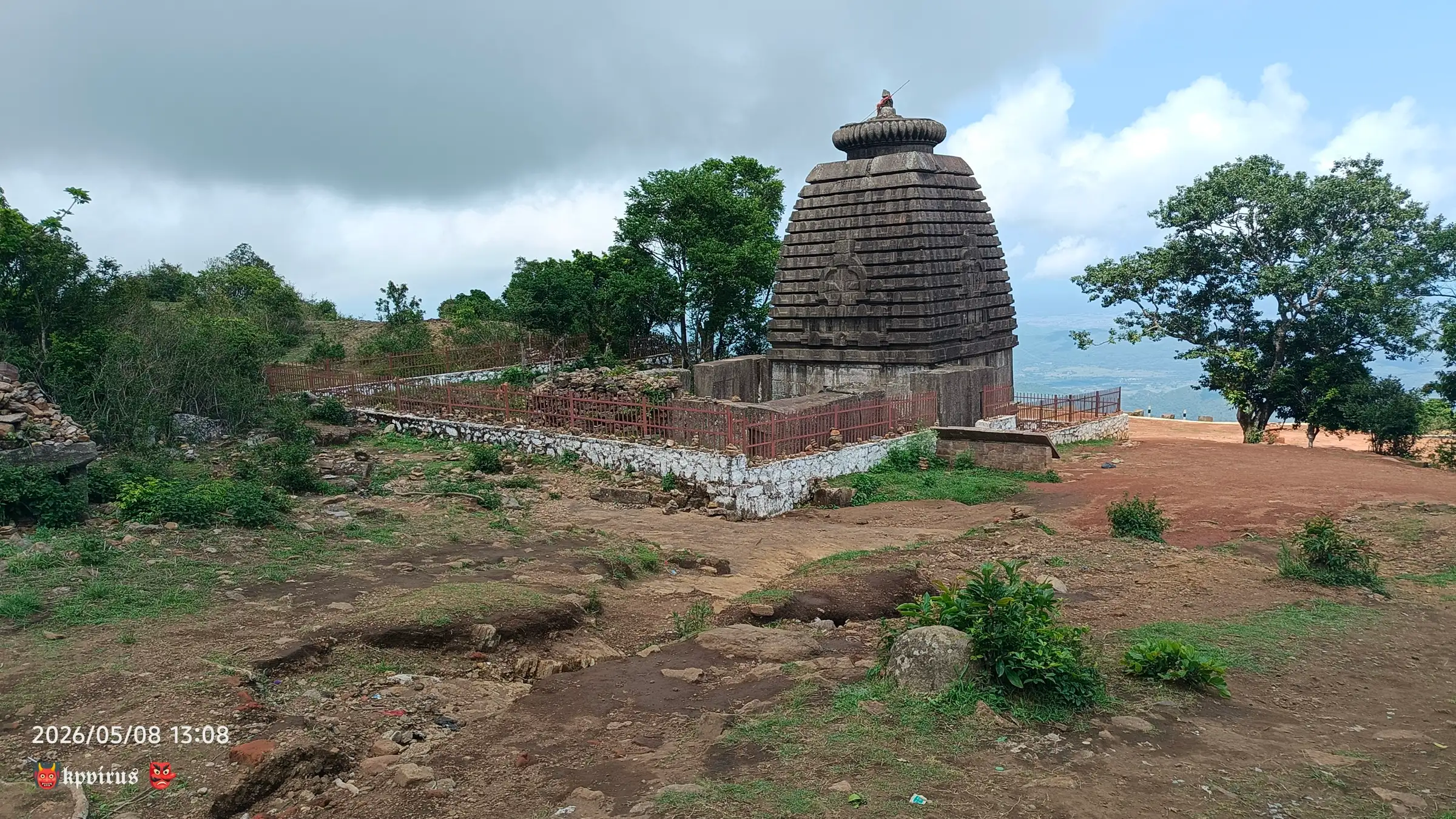 Ancient Kalinga-style stone temple with a rounded spire on the grassy Mahendragiri hilltop under a cloudy sky