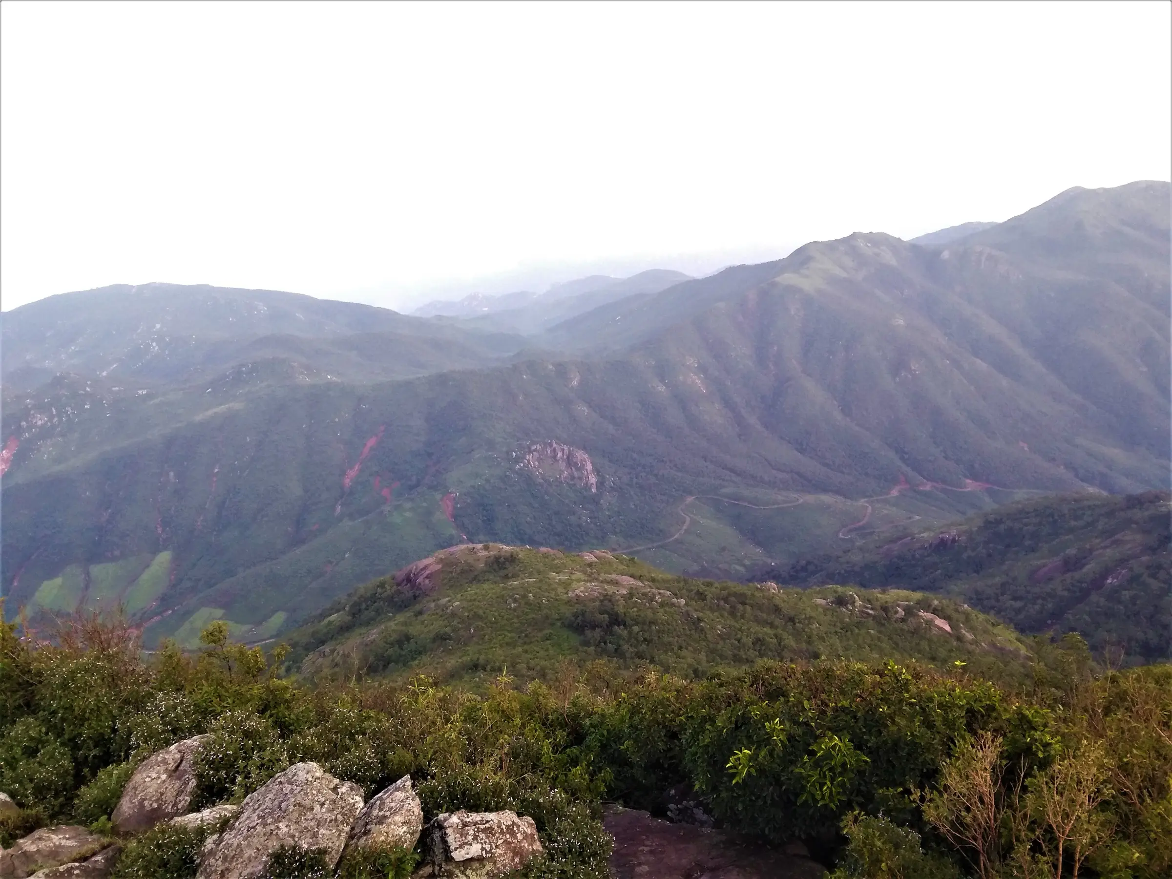 Green Eastern Ghats ridges and a winding road seen from the boulder-strewn summit area near the Bhima temple