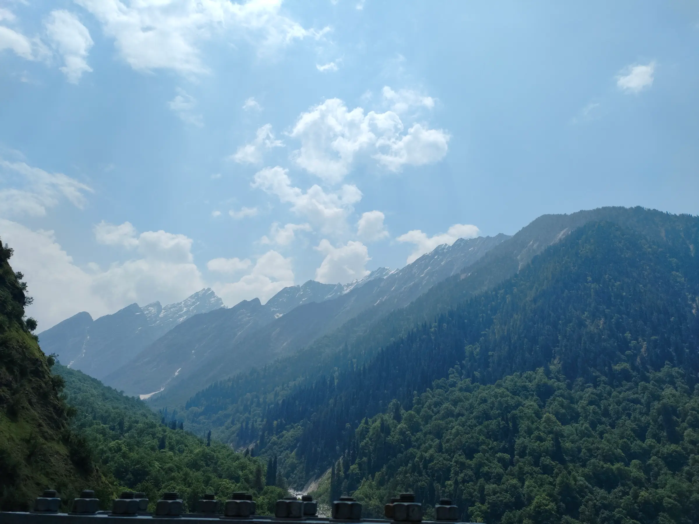 Forested Bhyundar valley with snow-streaked peaks at its head, seen from a bridge