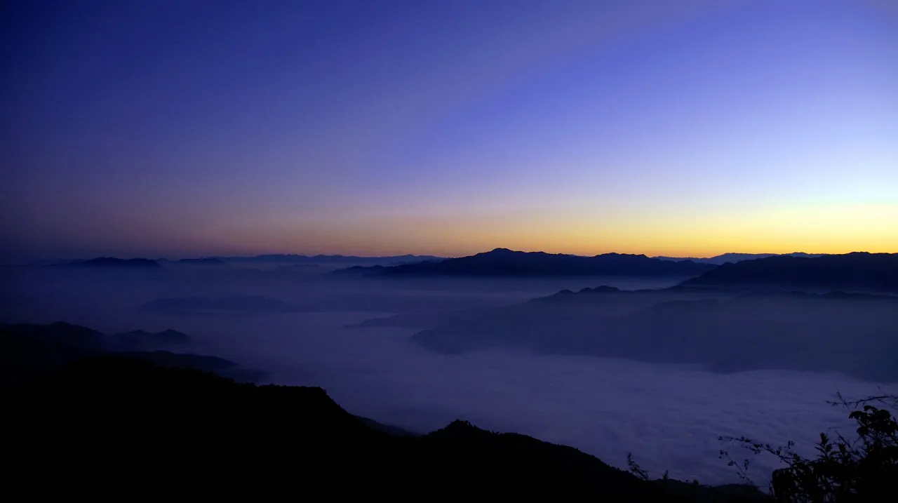Dawn over a sea of clouds and dark ridges seen from Blue Mountain National Park, Mizoram