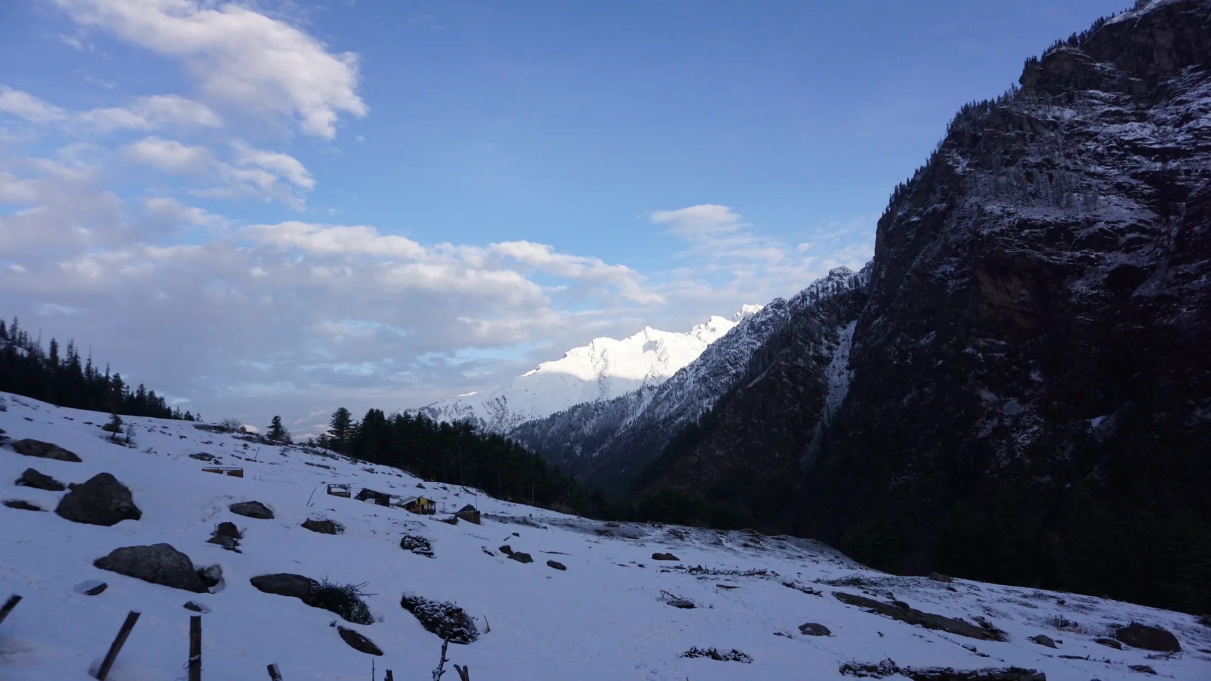 Snow-covered meadow at Kheerganga with a snow peak at the head of the Parvati valley and a dark rock face on the right