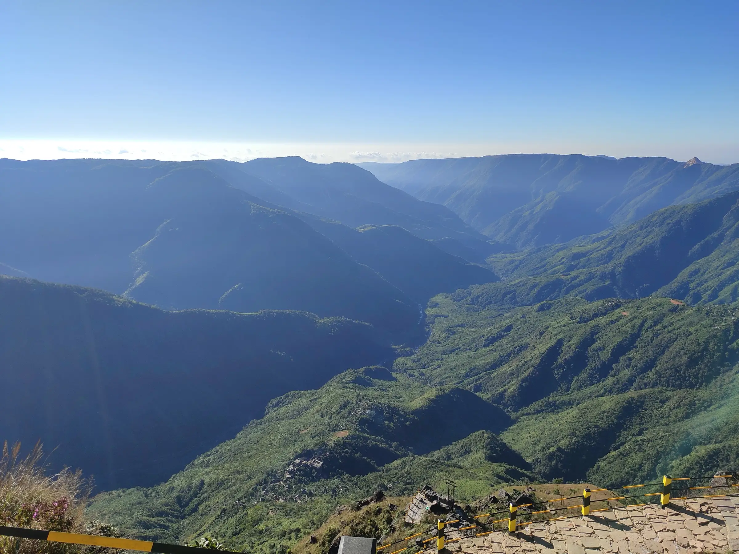 Layered green ridges and deep forested gorges of Laitlum Canyon under a clear blue sky, seen from the paved viewpoint on the rim