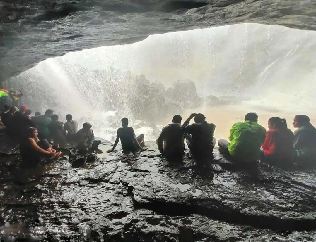 Trekkers sitting on wet rock in the eye-shaped cave behind the curtain of Kataldhar Waterfall