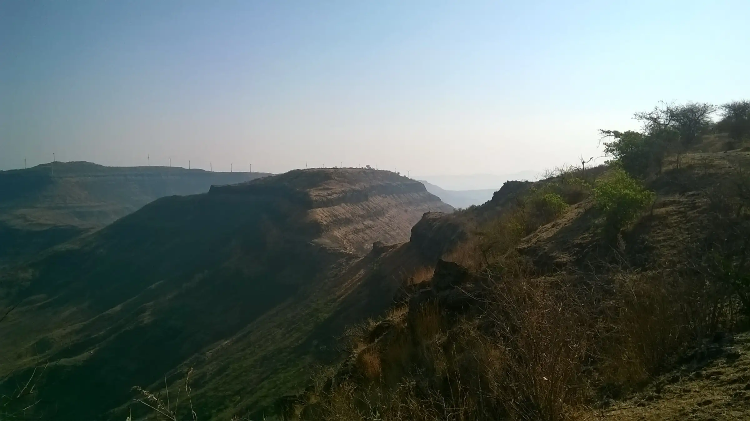 Flat-topped Chandan Fort seen from Vandan Fort, with wind turbines on the ridge behind