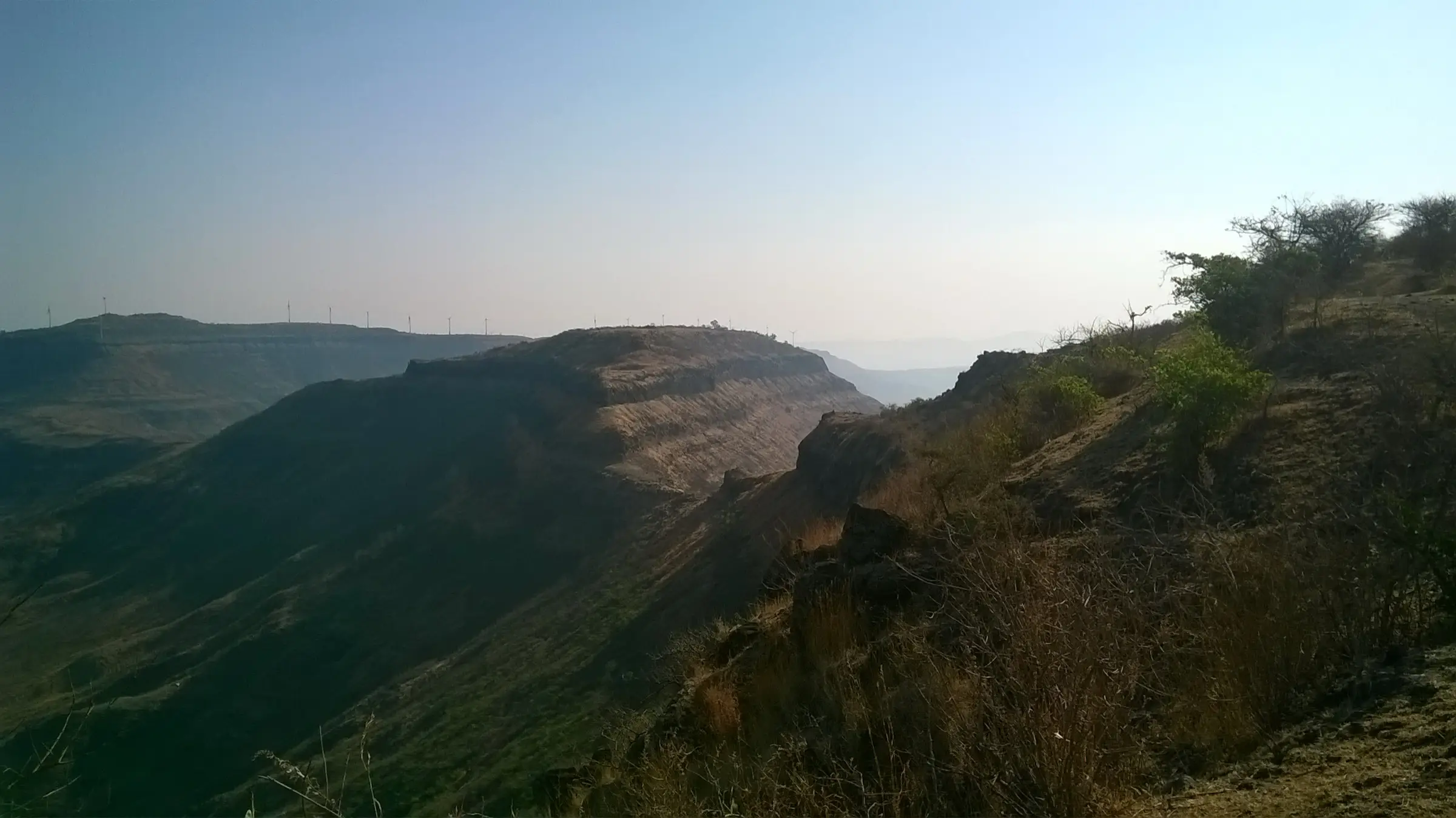 Flat-topped Chandan Fort seen from Vandan Fort, with wind turbines on the ridge behind