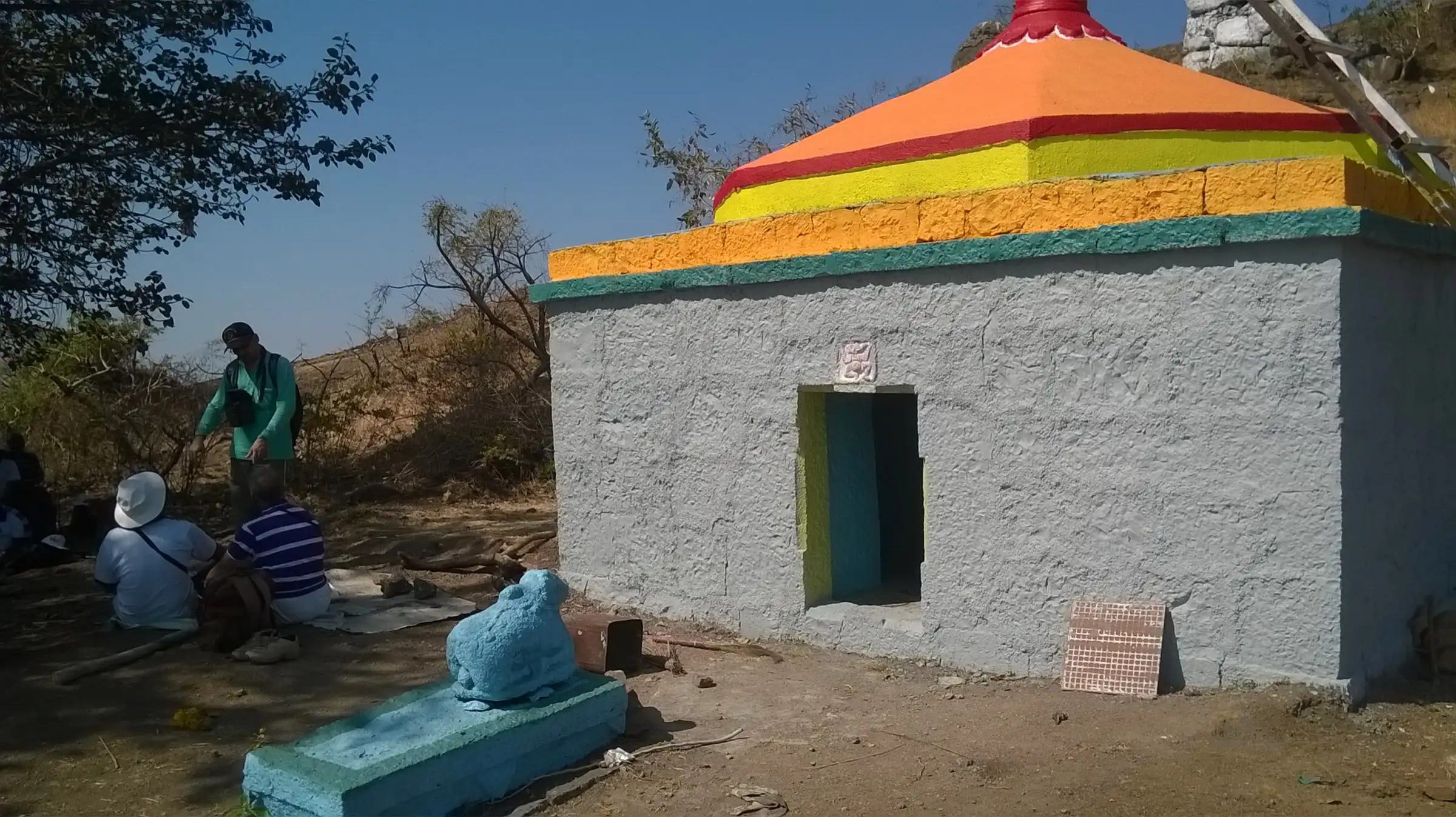 Freshly painted Mahadev mandir on Chandan Fort with a Nandi in front and trekkers resting in the shade