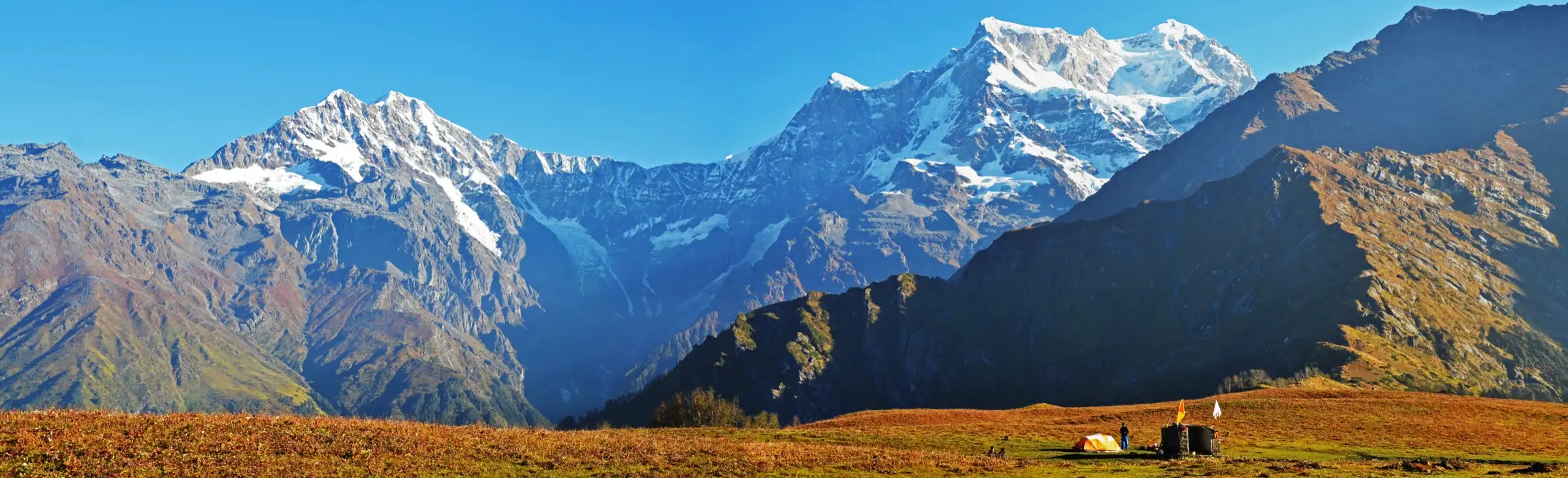 Snow-covered Chaukhamba massif rising above an autumn meadow with a small tent and shrine at Budha Madhyamaheshwar, near the end of the Panpatia Col route
