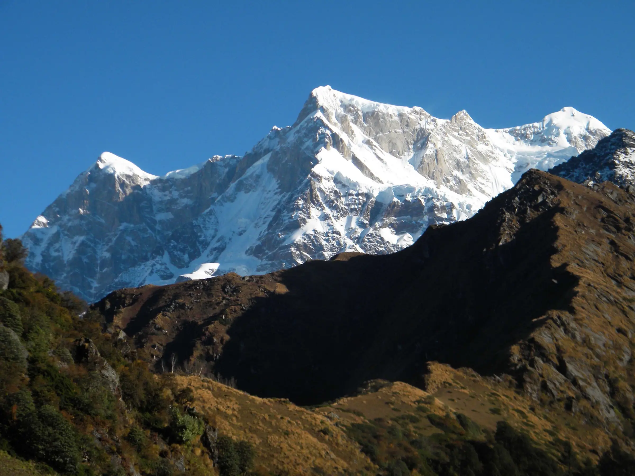 Chaukhamba peaks rising above brown autumn ridges, seen from the trail above Madmaheshwar Temple