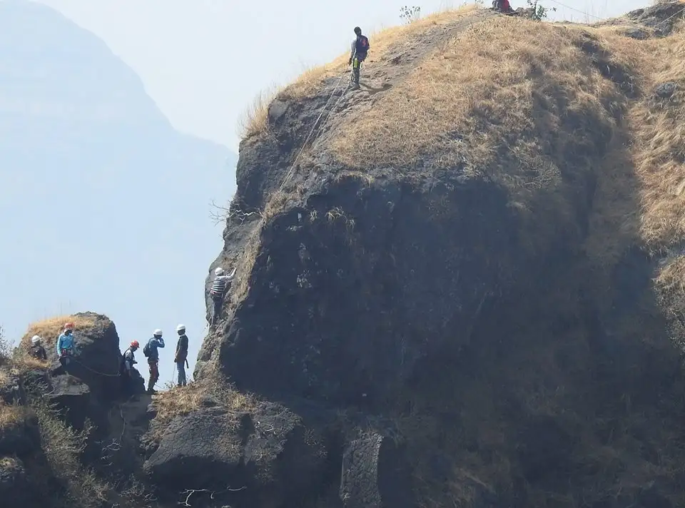Climbers in helmets roped up on a rock pitch on Lingana with a belayer on the grassy ledge above