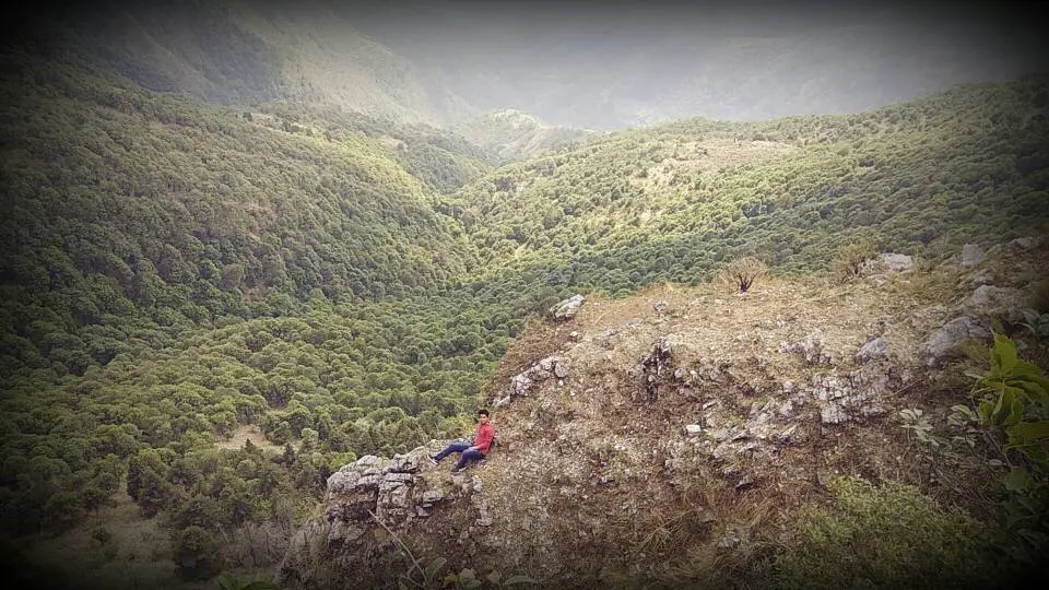 A hiker sitting on a rocky spur above deep oak-forested valleys near Cloud End, Mussoorie