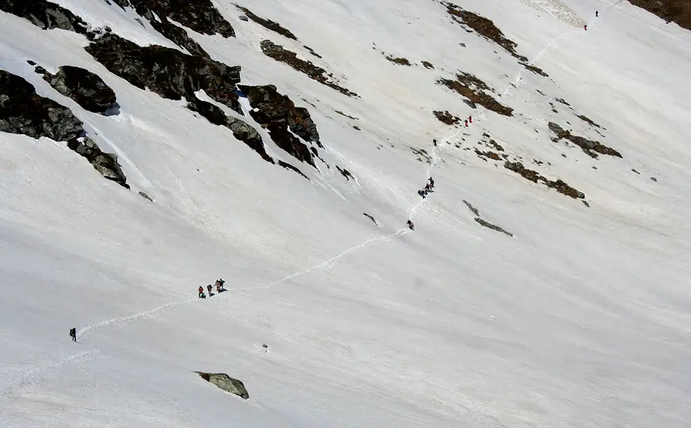 A line of trekkers crossing a wide snow slope on the way over Sar Pass