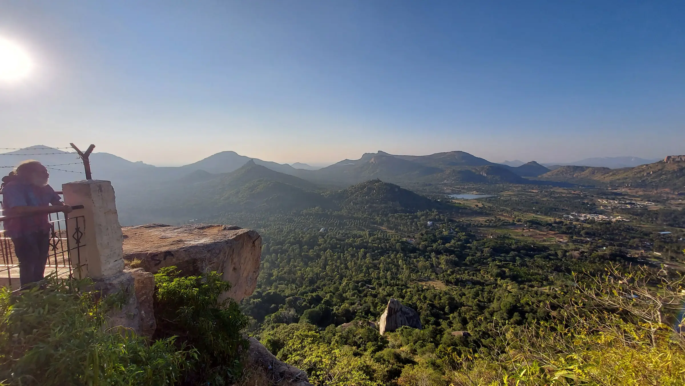 View of the Devarayanadurga hills near the Minchukallu Betta trek: forested valleys, a small lake and rocky ridges under a clear sky (not the trek itself)