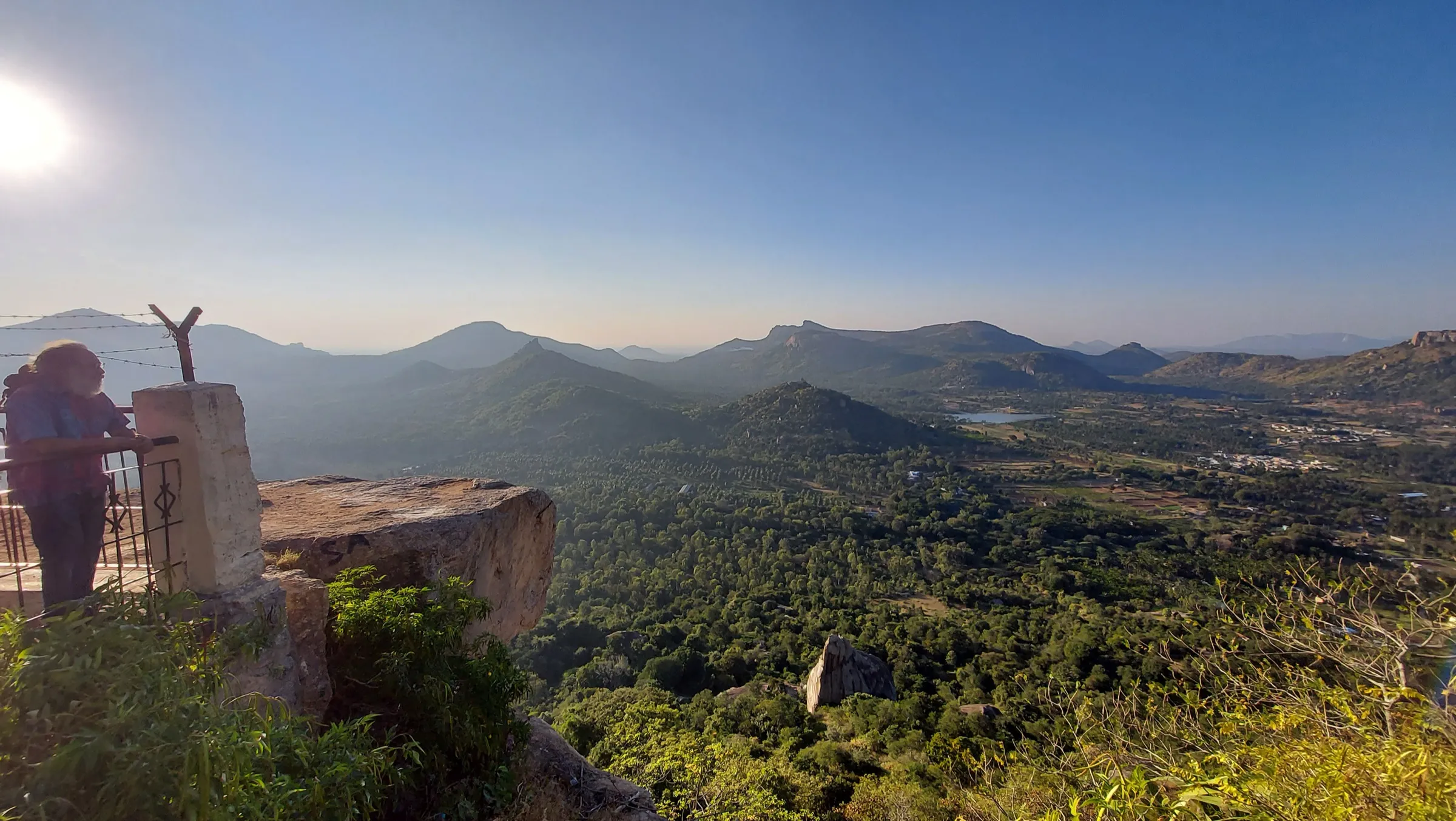 View of the Devarayanadurga hills near the Minchukallu Betta trek: forested valleys, a small lake and rocky ridges under a clear sky (not the trek itself)