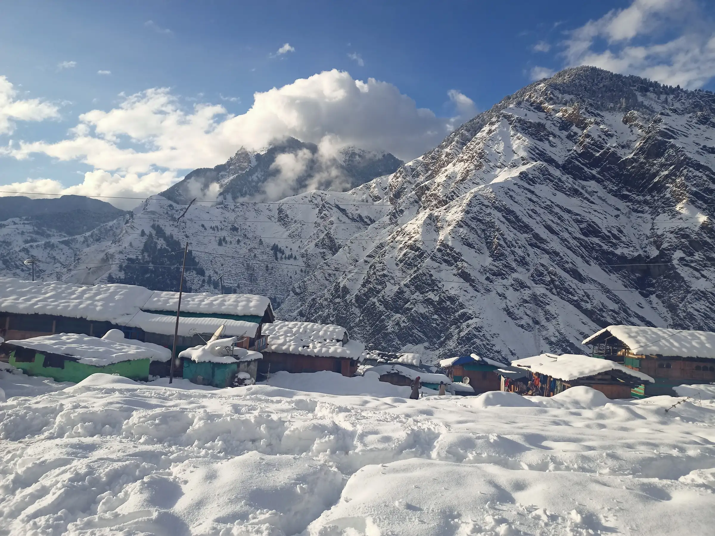 Snow-covered wooden houses of Dhara village below a steep snowy mountain in the Supin valley