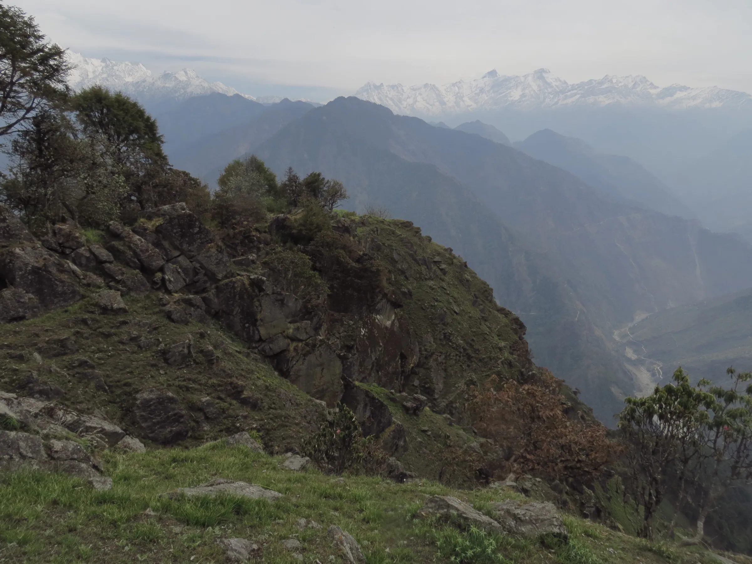 Rocky forested ridges above a deep valley, with a line of snow peaks on the horizon, in the hills around Dharchula where the Chipla Kedar trek starts
