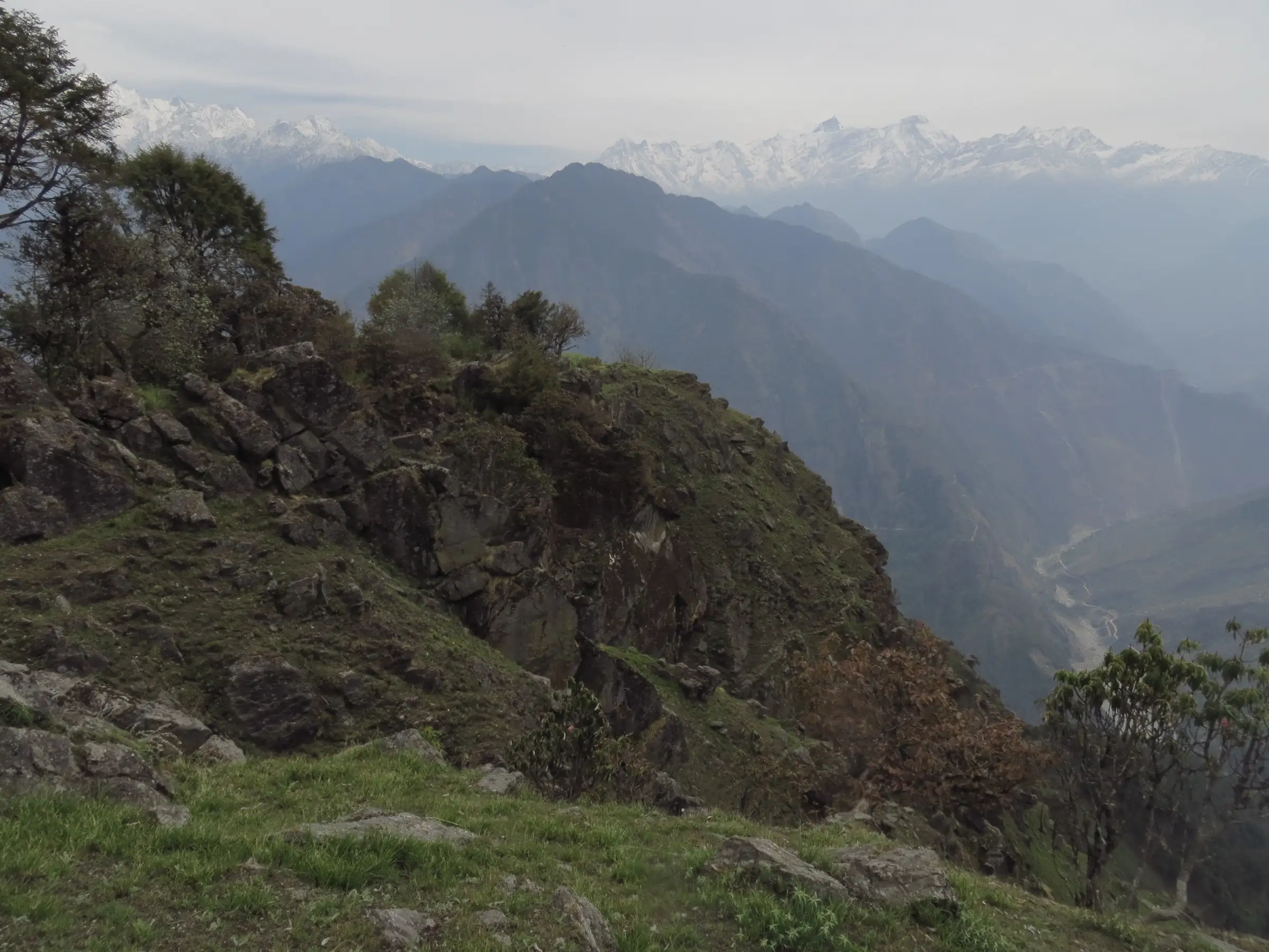 Rocky forested ridges above a deep valley, with a line of snow peaks on the horizon, in the hills around Dharchula where the Chipla Kedar trek starts
