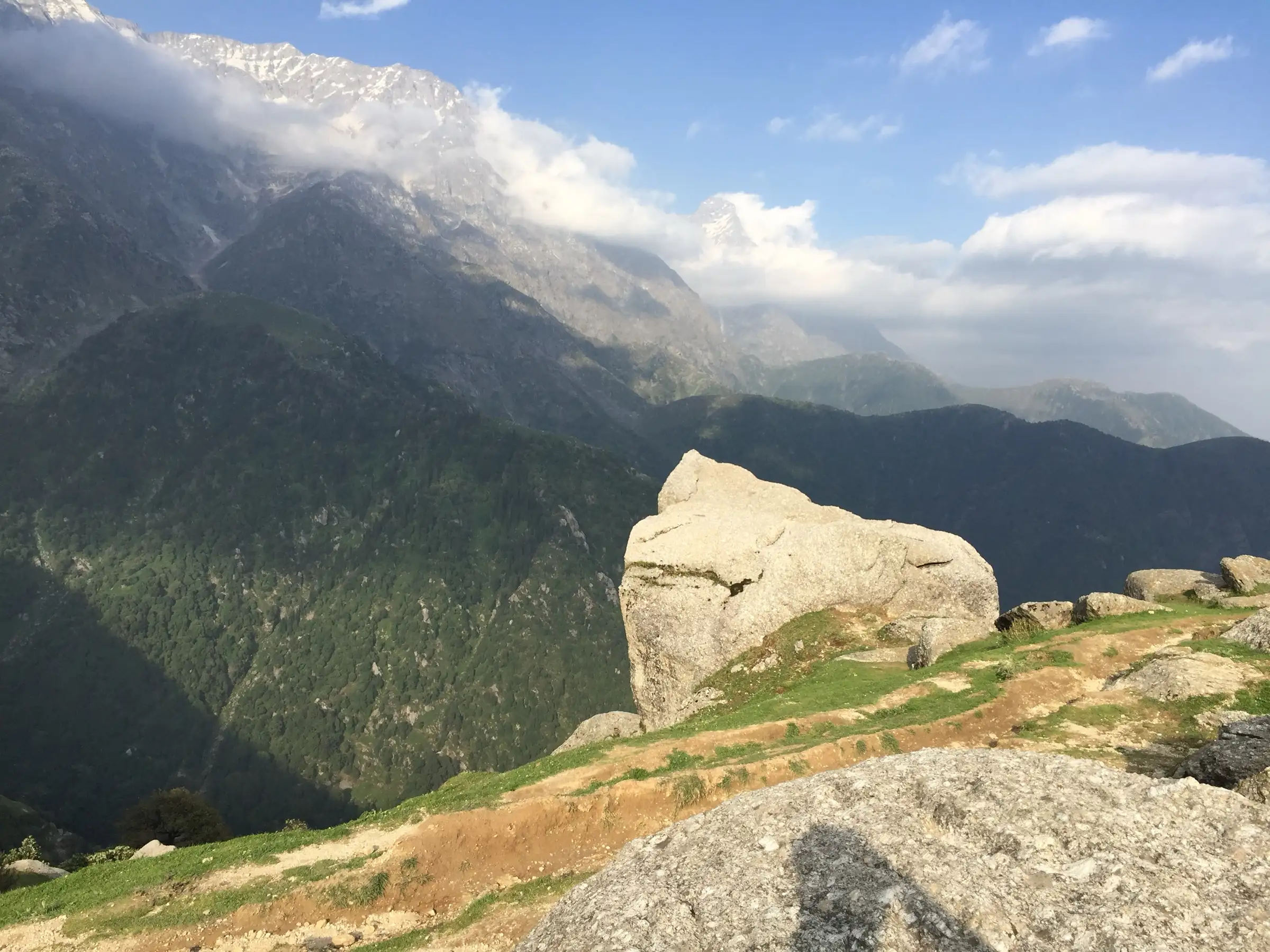 Snow-streaked Dhauladhar peaks and forested slopes seen from the boulder-strewn Triund ridge