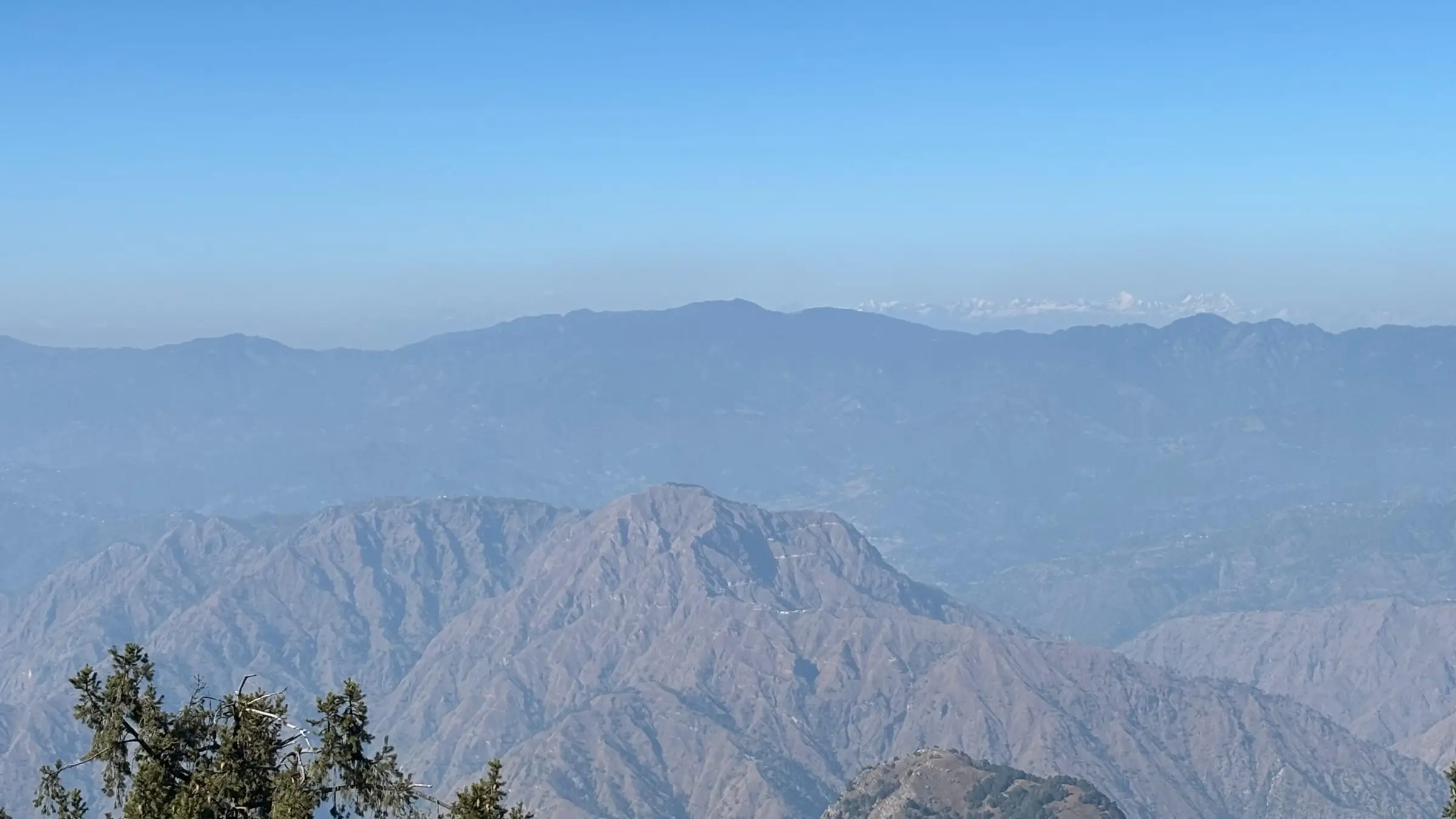 Hazy layered ridges of Shimla district with a faint line of snow peaks on the horizon, seen from the Shali Mata Temple