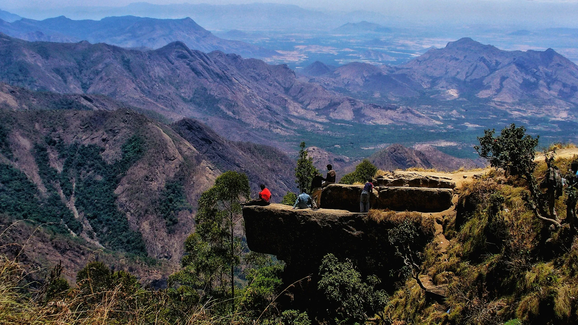Trekkers on the rock ledge of Dolphin's Nose near Vattakanal, the first big viewpoint on the walk down to Vellagavi, with the Palani Hills beyond