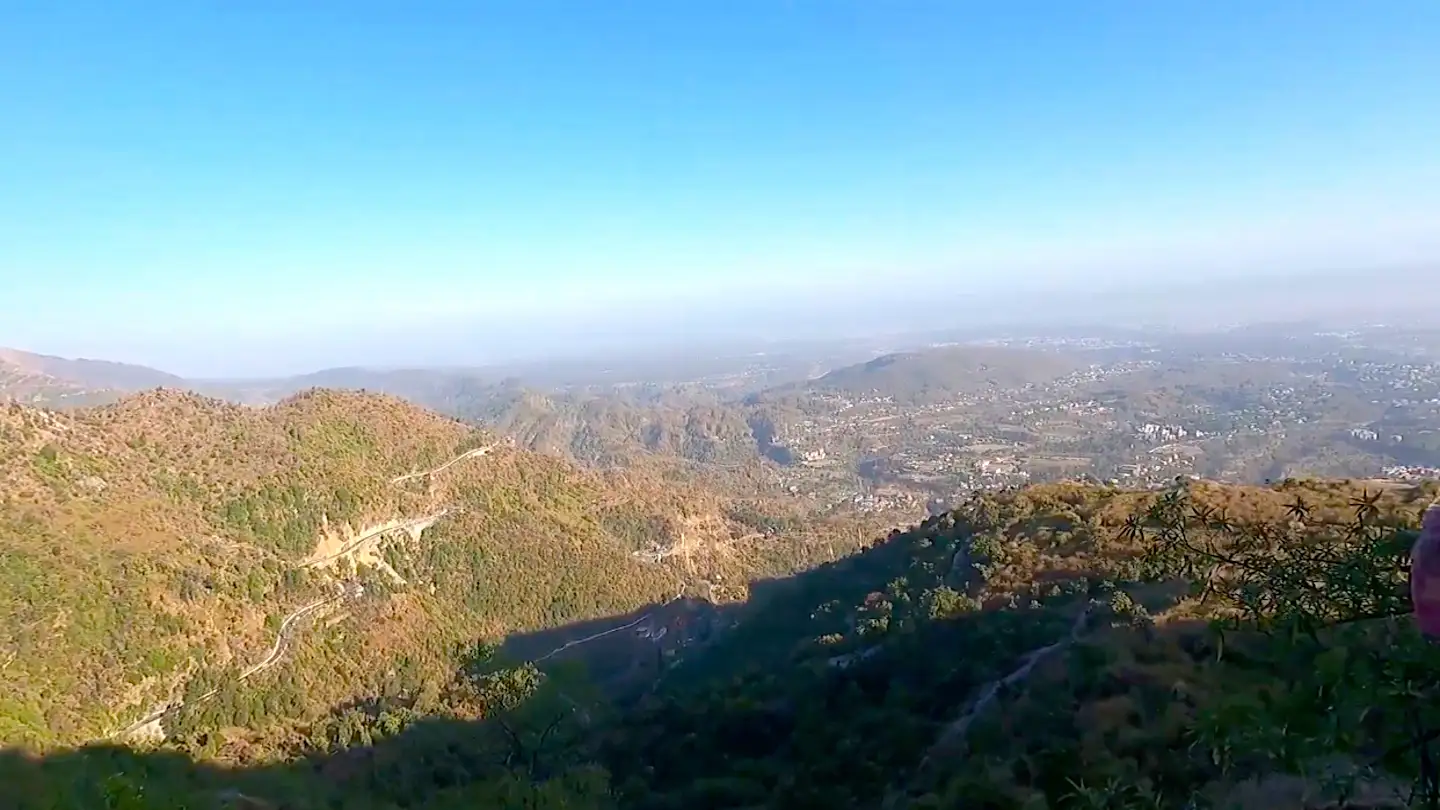 Wide view over forested foothills and the hazy Doon Valley with winding roads, seen from the Kipling Trail