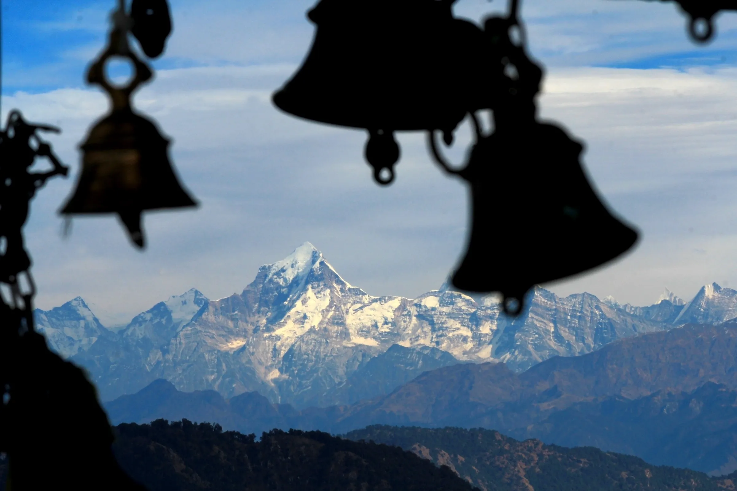 Dunagiri peak and snowy Garhwal ranges framed by the silhouettes of temple bells at Kartik Swami
