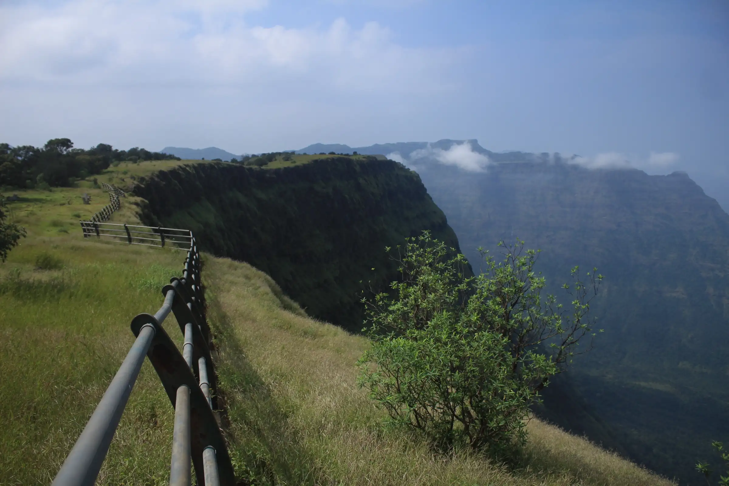 Fenced grassy path along the edge of the escarpment near Durgawadi, with steep cliffs and green valleys falling to the Konkan