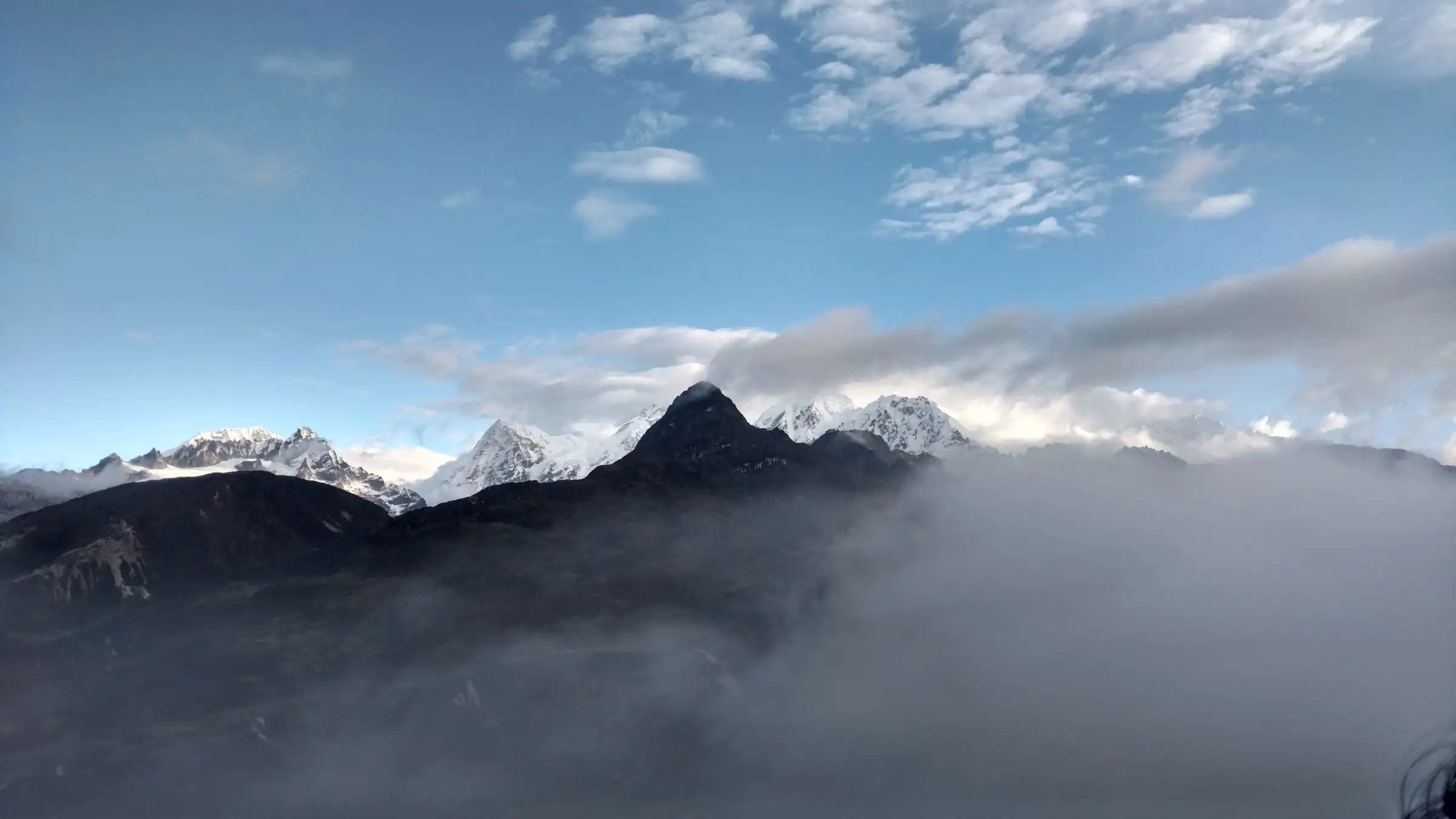 Dark rocky peak and snowy Himalayan summits rising out of drifting cloud above Dzongri