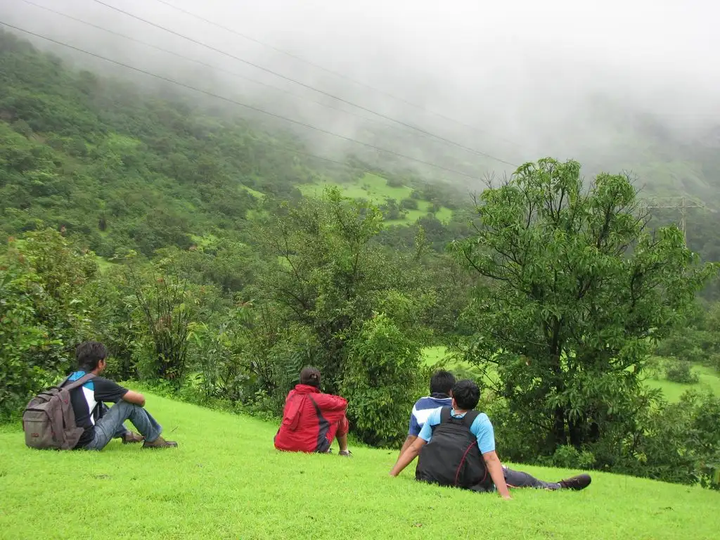 Four trekkers resting on green grass on the way to Duke's Nose as monsoon mist covers the hills