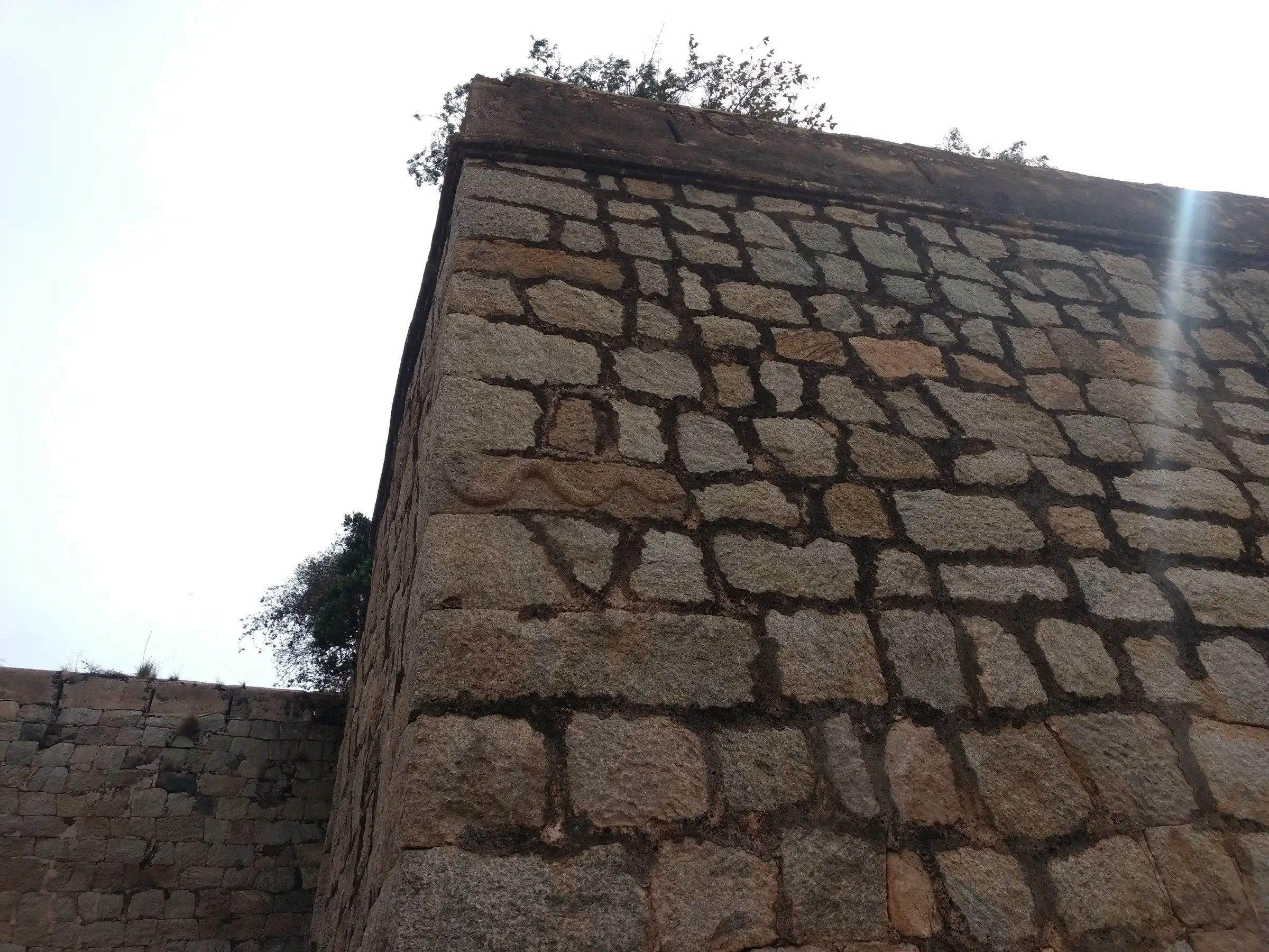 Dressed-stone wall at the entrance of Channarayana Durga fort with a carved snake on one block