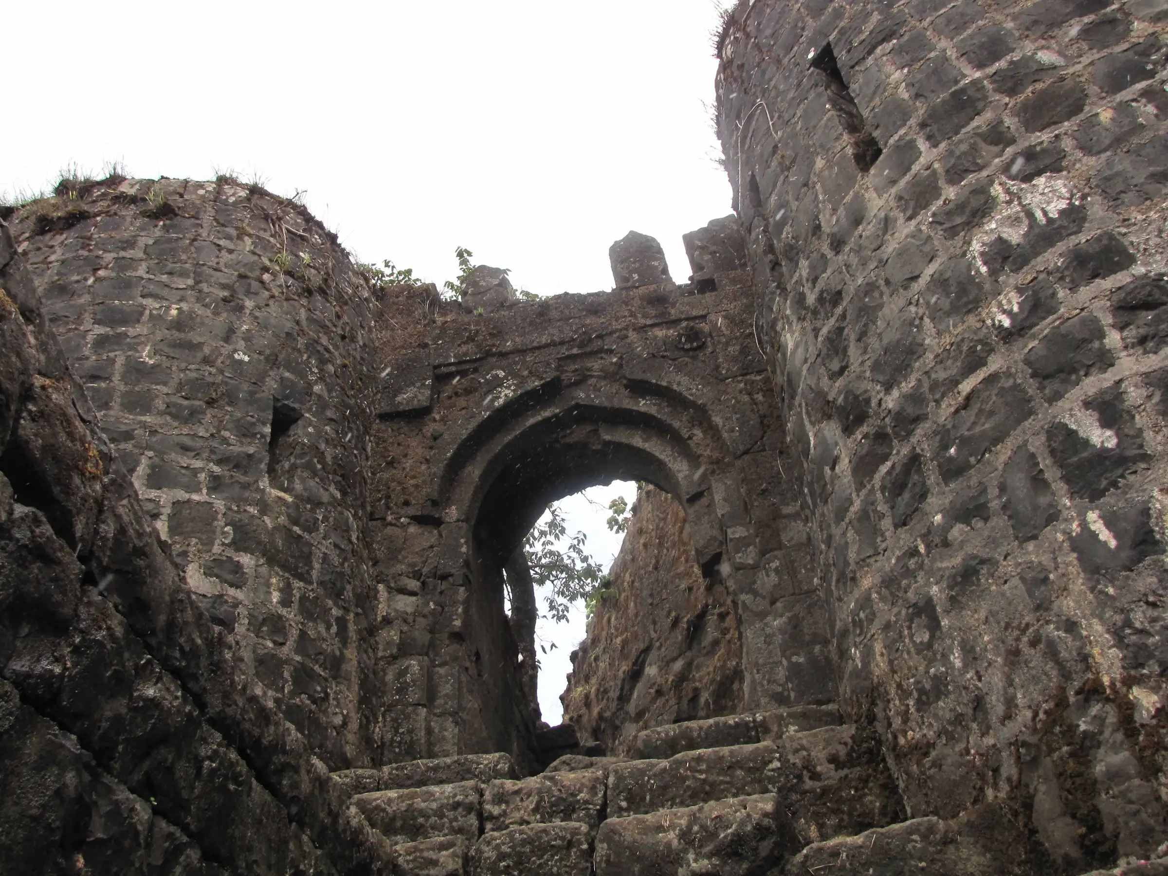 Stone steps leading up through the arched entrance gate of Tikona Fort between two bastions