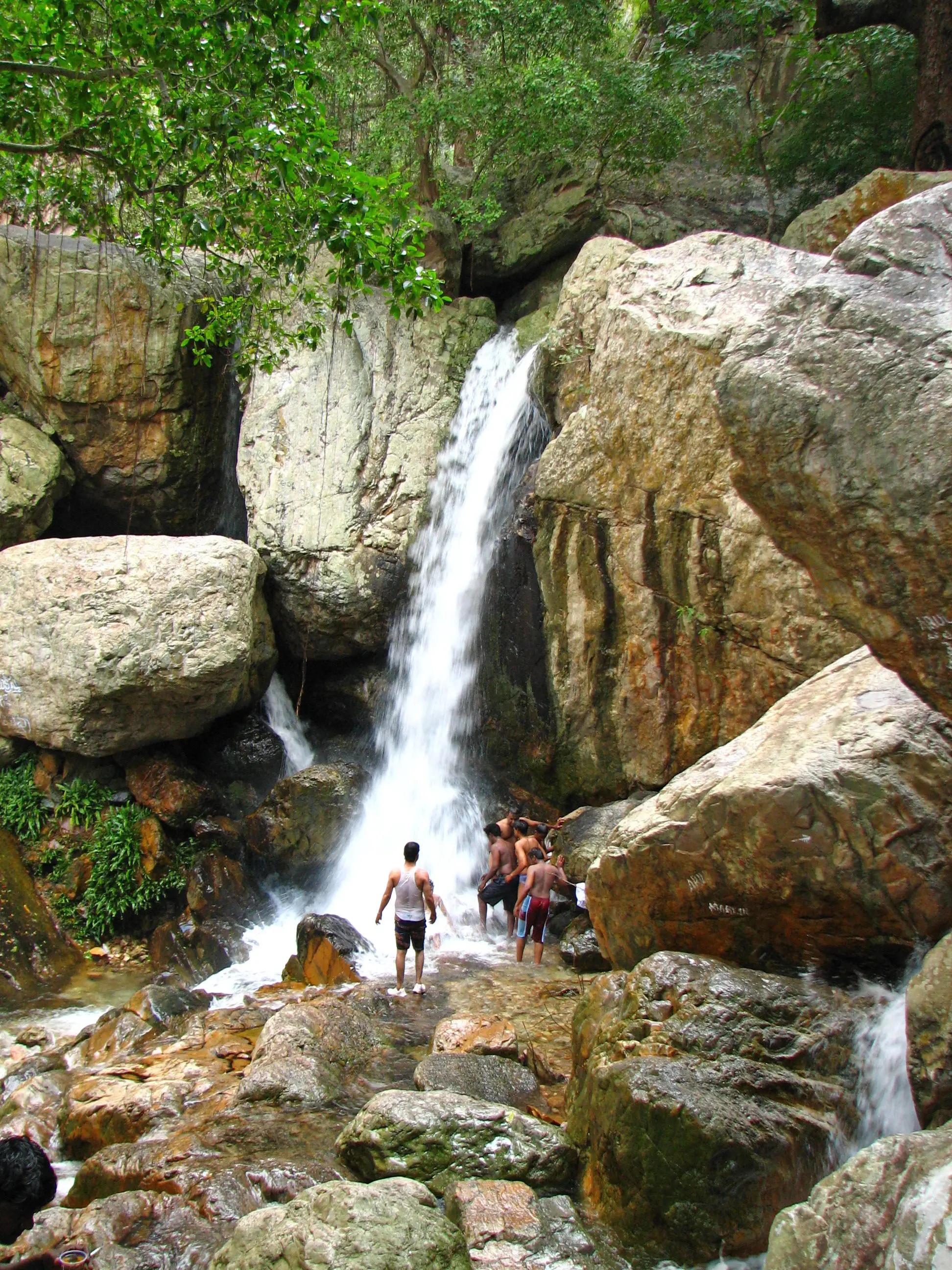 The first Tada waterfall pouring between huge granite boulders as bathers stand in its spray