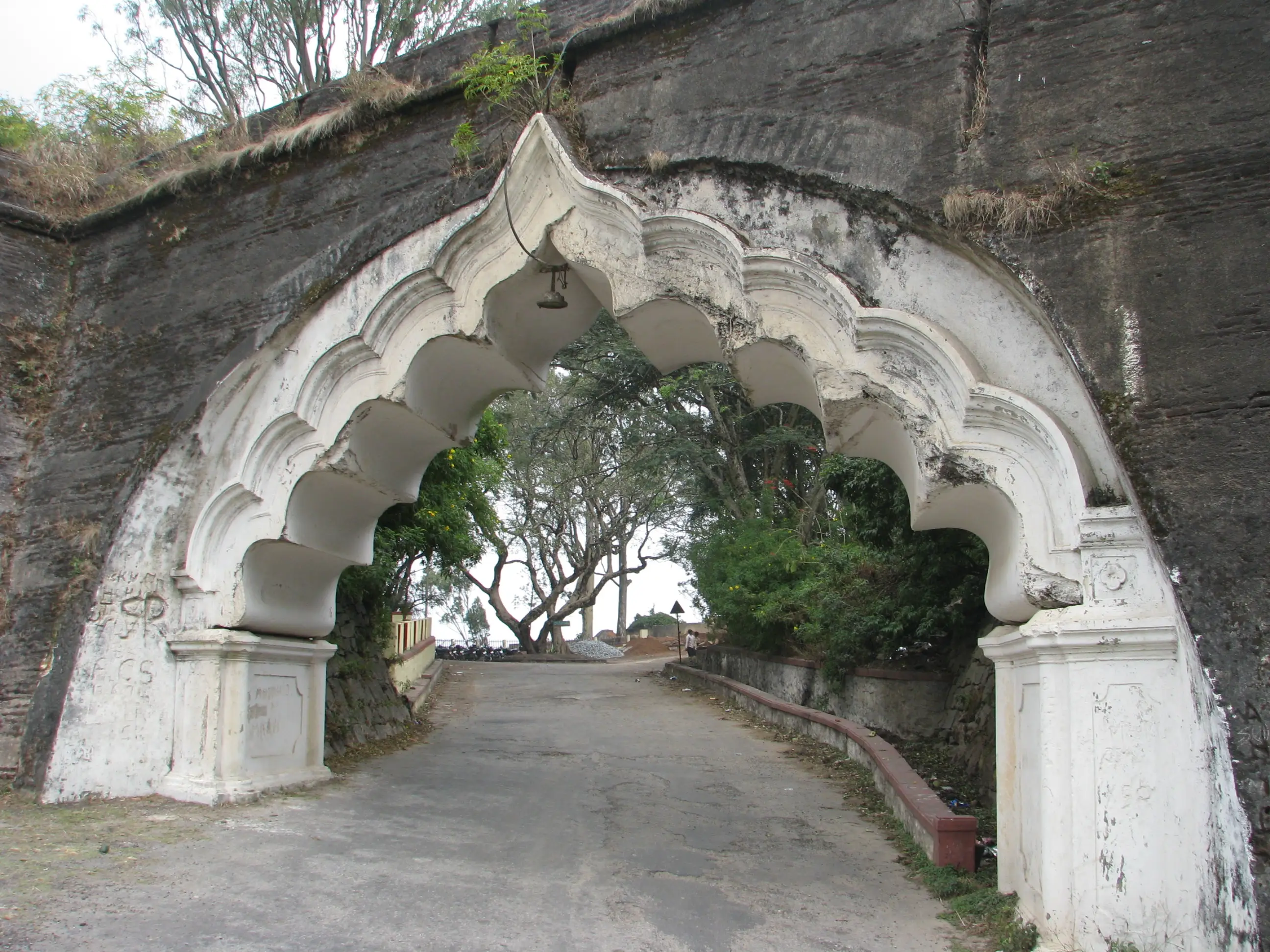 White scalloped stone archway in the dark granite wall of the Nandi Hills fort