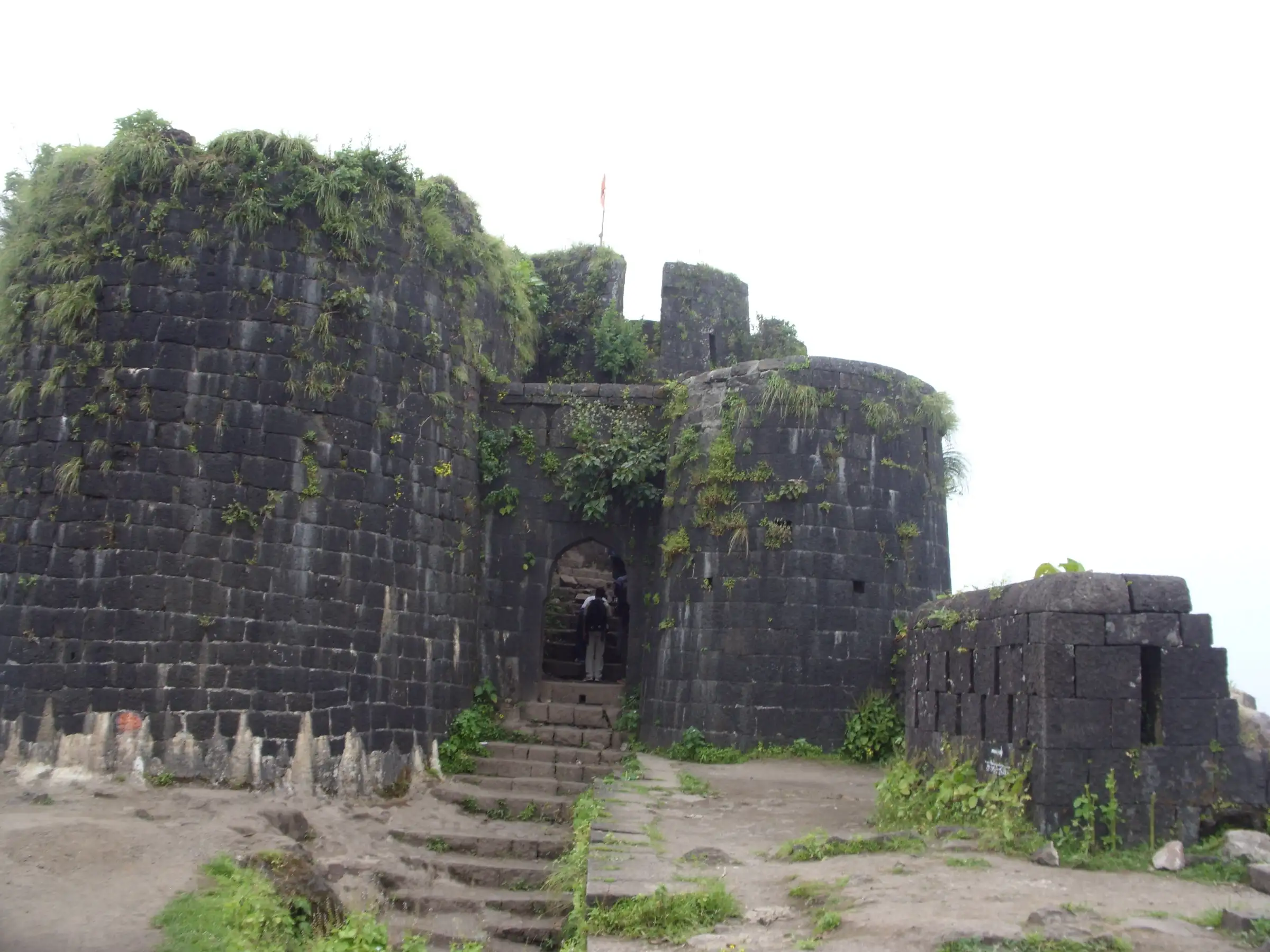 Stone steps leading up to an arched gate between two dark basalt bastions on Purandar Fort