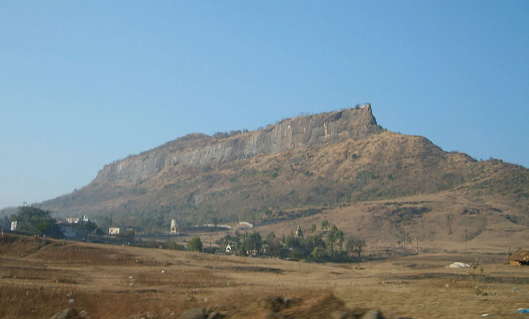 The long cliff-girt hill of Shivneri Fort rising above dry fields and the edge of Junnar town